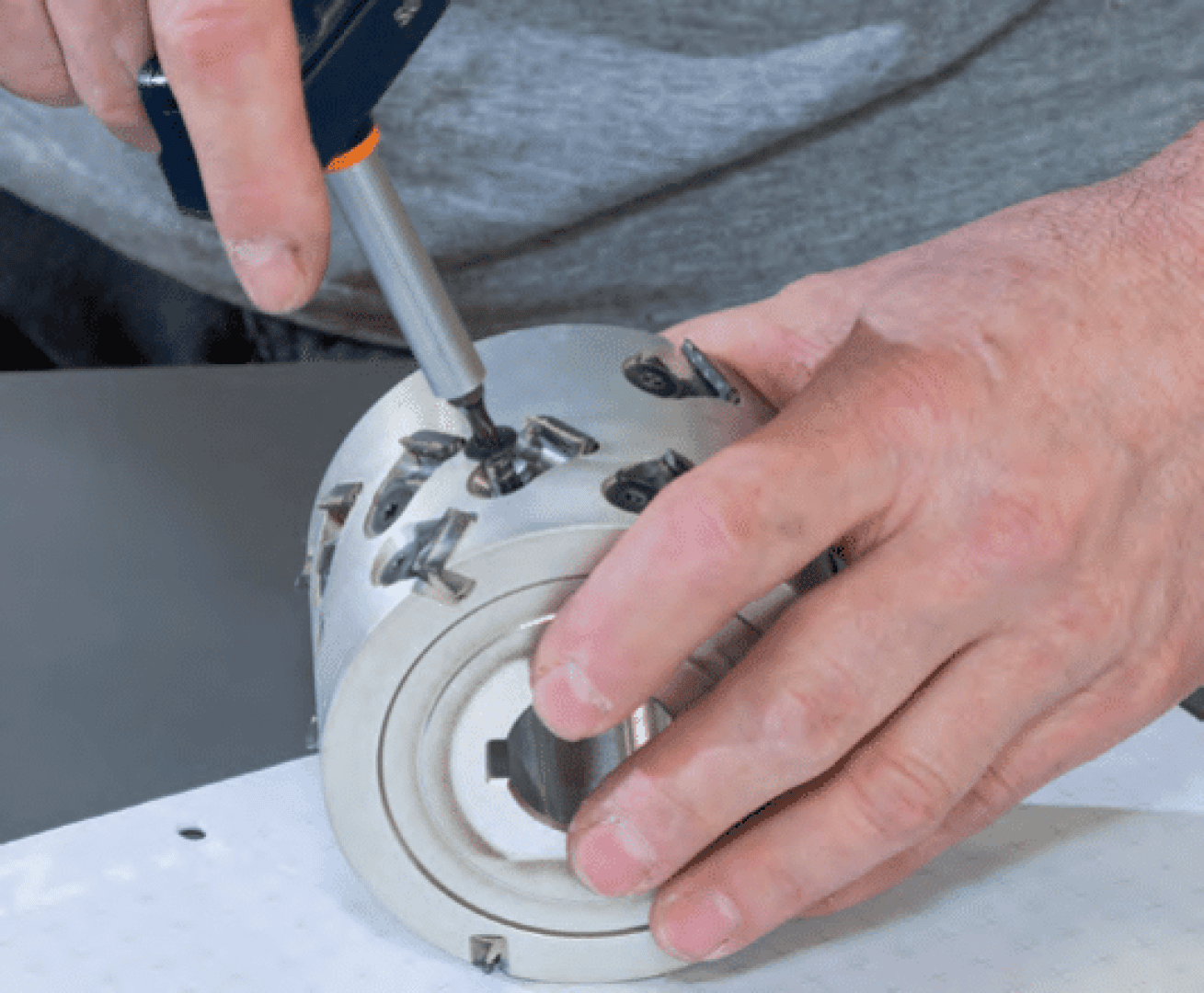 Eine Person verwendet einen Schraubendreher, um eine Schraube an einem Metallschneidewerkzeug oder einem Fräser festzuziehen oder einzustellen, und hält ihn mit einer Hand auf einer Werkbank fest.