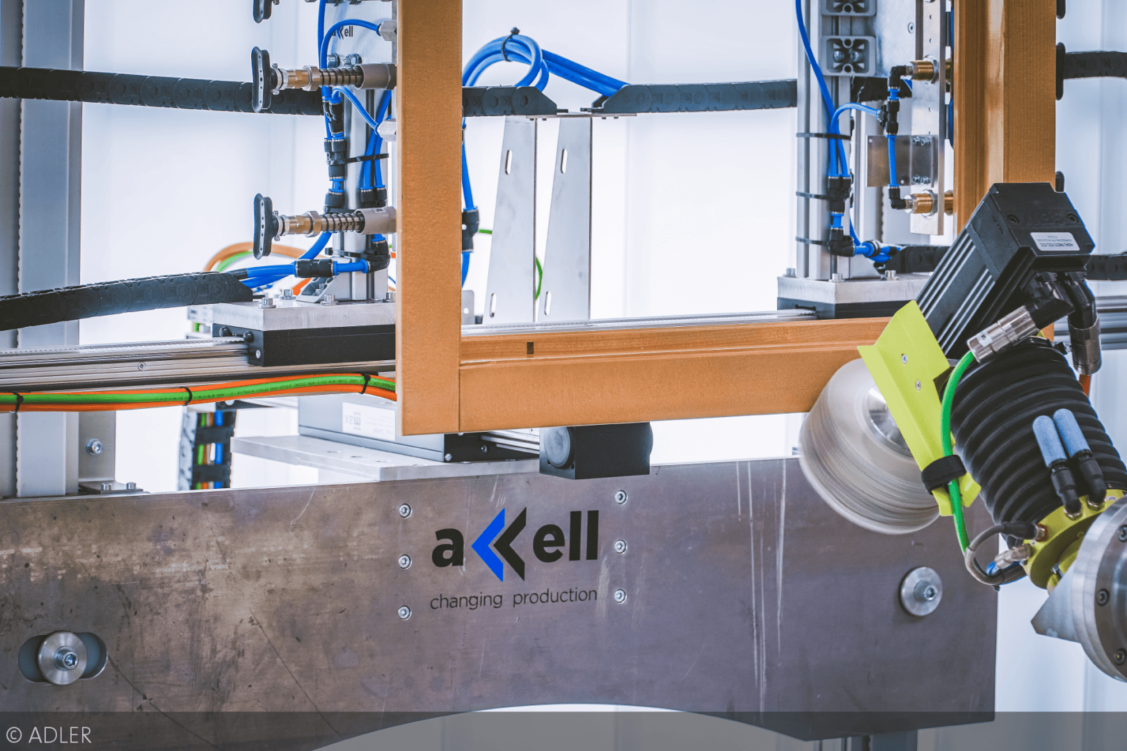 Nahaufnahme einer automatisierten Maschine mit Drähten, Schläuchen und Metallteilen, mit dem Axell-Logo für wechselnde Produktion auf einer Metallplatte.