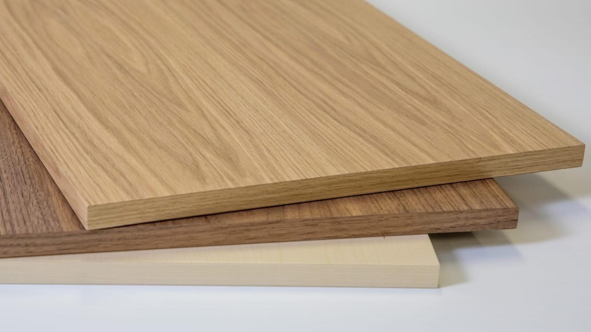 Trois planches de bois de couleurs et de motifs différents sont empilées sur une surface claire. La planche du haut est marron clair, celle du milieu est marron moyen et celle du bas est beige clair.