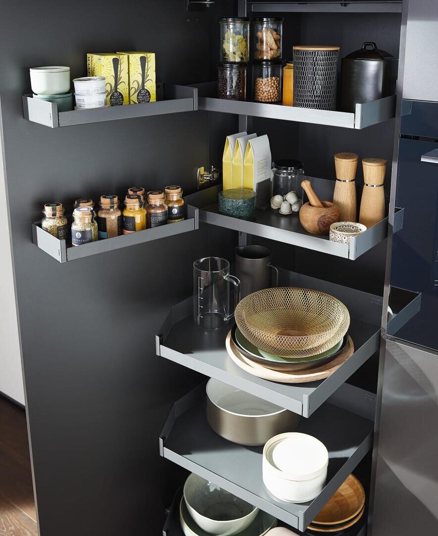Ein moderner Küchenschrank mit ausziehbaren Fächern, in denen Gewürze, Gläser, Öle, Holzbehälter, Schüsseln, Teller und Tassen in einem grauen Innenraum übersichtlich angeordnet sind.