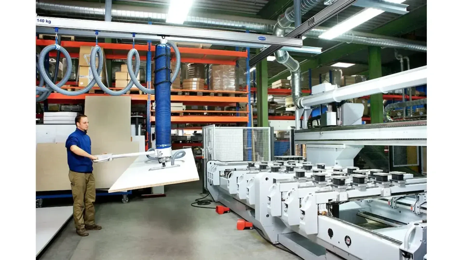 Un ouvrier fait fonctionner une grande machine automatisée qui manipule une feuille de matériau dans une usine industrielle moderne, avec des étagères de fournitures et d'équipements à l'arrière-plan.