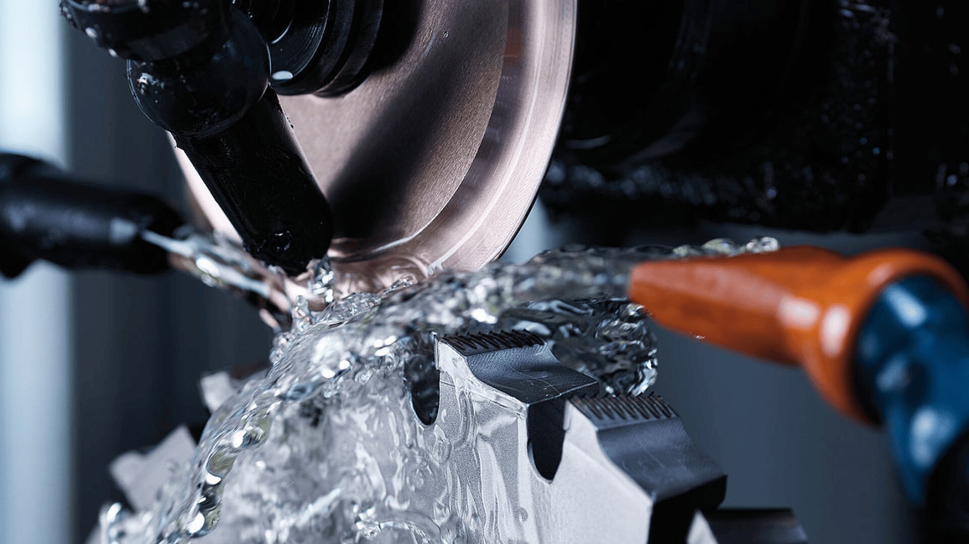 Nahaufnahme einer kreisförmigen Schleifscheibe, die ein Metallschneidwerkzeug schärft, wobei Kühlflüssigkeit auf das Werkzeug gesprüht wird, um Hitze und Reibung während des Bearbeitungsprozesses zu verringern.