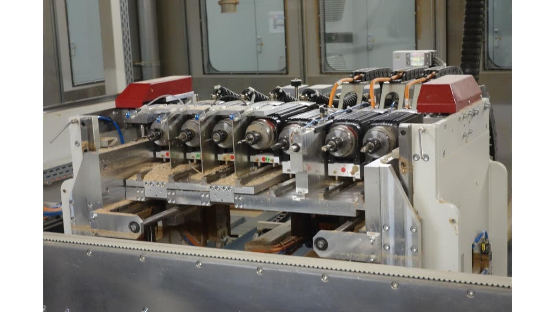 Gros plan d'une machine à bois industrielle dotée de plusieurs têtes rotatives, de moteurs électriques et de boutons de commande, traitant des planches de bois dans une usine.
