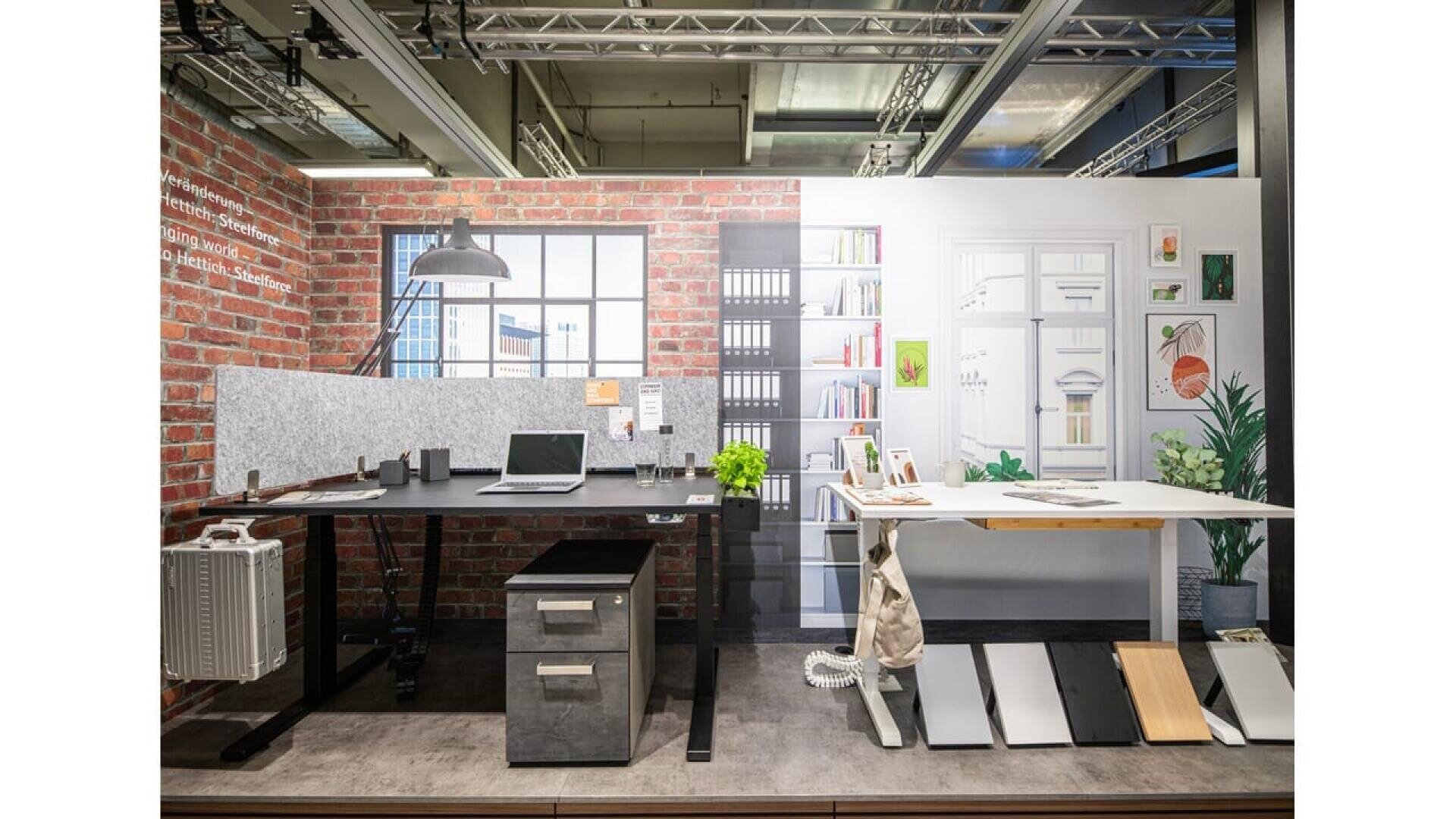 Bureau moderne composé d'un bureau noir avec un ordinateur portable, une lampe et des plantes, d'un mur de briques en toile de fond, d'une grande fenêtre, d'étagères avec des livres et d'un bureau debout avec des outils de dessin et des échantillons.