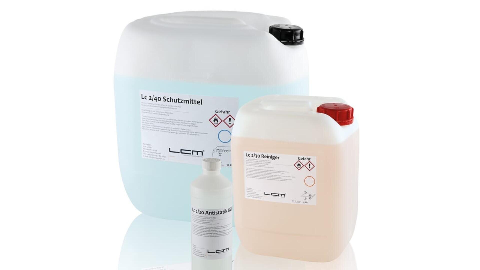 Trois récipients en plastique de tailles différentes, munis d'étiquettes allemandes et de symboles de danger, contenant diverses solutions de nettoyage et de protection, sont disposés sur un fond blanc.