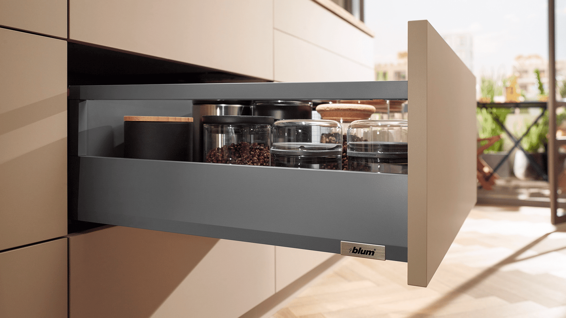 Eine moderne Küchenschublade, die teilweise geöffnet ist und Gläser und Behälter mit verschiedenen Lebensmitteln enthält. Die Schublade hat ein schlichtes, minimalistisches Design mit einem Blum-Markenetikett.