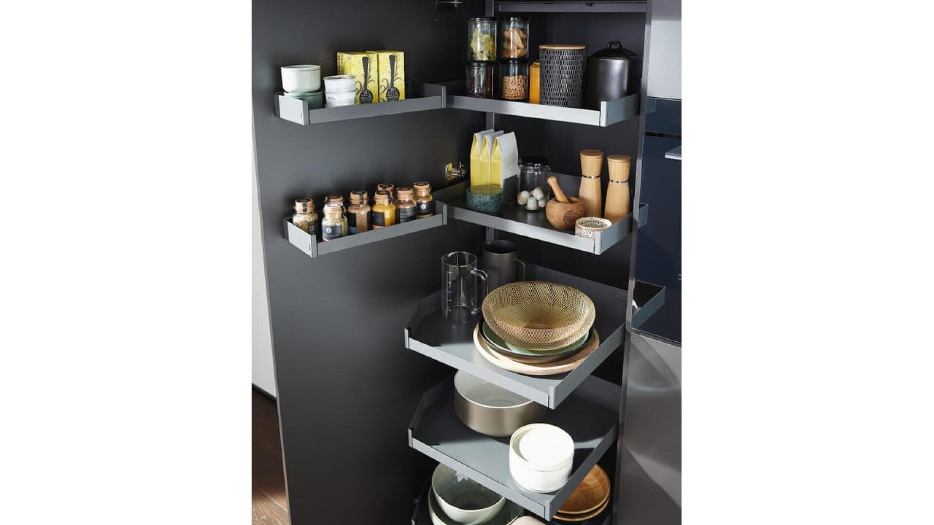Garde-manger d'angle ouvert avec plusieurs étagères grises présentant divers articles, notamment des bocaux en verre, des récipients à épices, des bols, des assiettes, des bouteilles d'huile, des mugs, des moulins à sel et à poivre et des boîtes à thé, le tout bien rangé.
