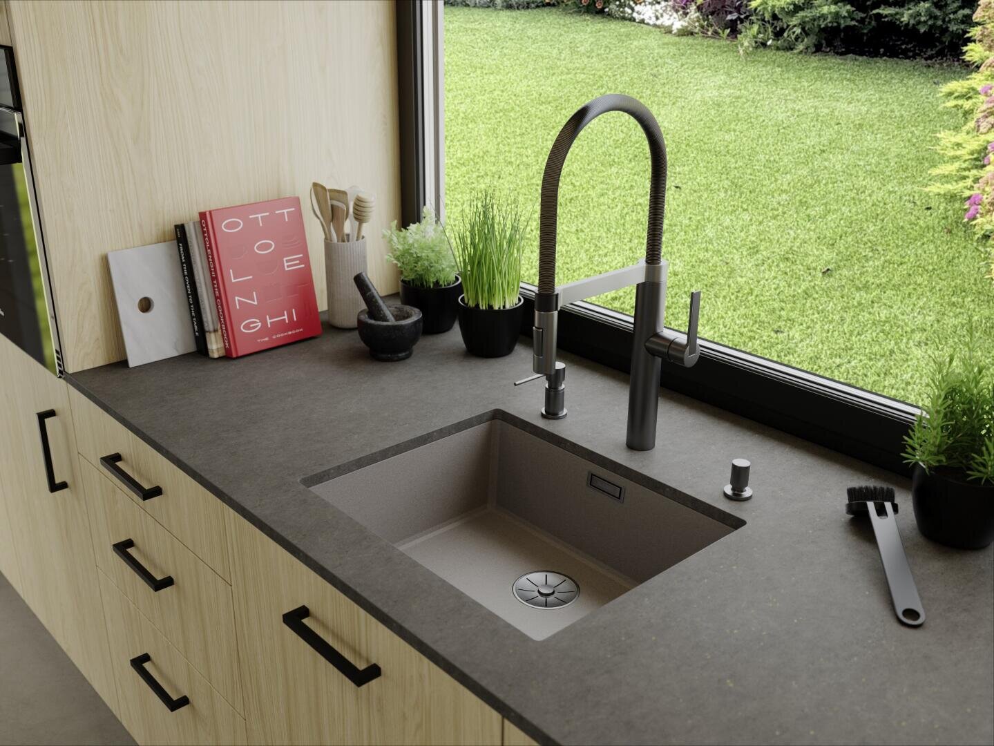 Un plan de travail de cuisine moderne avec un évier, un robinet noir, des plantes en pot, des ustensiles, un livre et une brosse se trouve près d'une grande fenêtre donnant sur une pelouse et un jardin verdoyants.