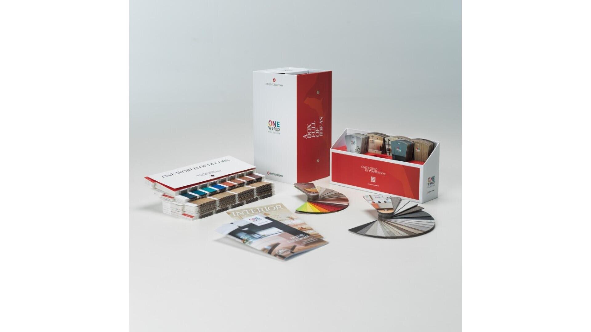 Un ensemble de kits d'échantillons de décoration intérieure comprenant des échantillons de couleurs, des échantillons de matériaux dans des boîtes, un éventail d'éclats de peinture, un livret et un magazine disposés sur une surface blanche.