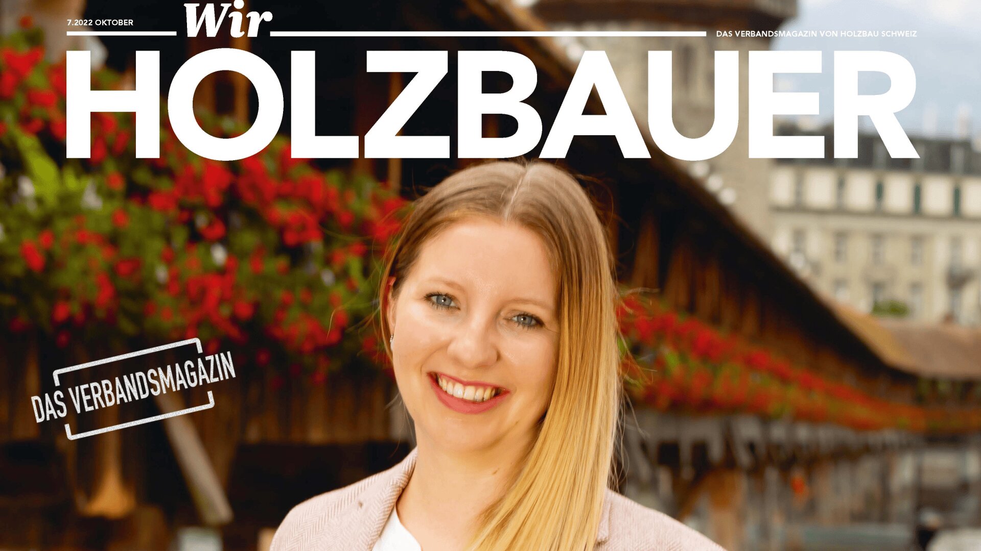 Eine lächelnde Frau mit langen blonden Haaren steht vor einer Holzbrücke. Über ihr erscheint der Zeitschriftentitel Wir HOLZBAUER, links davon der Untertitel DAS VERBANDSMAGAZIN.