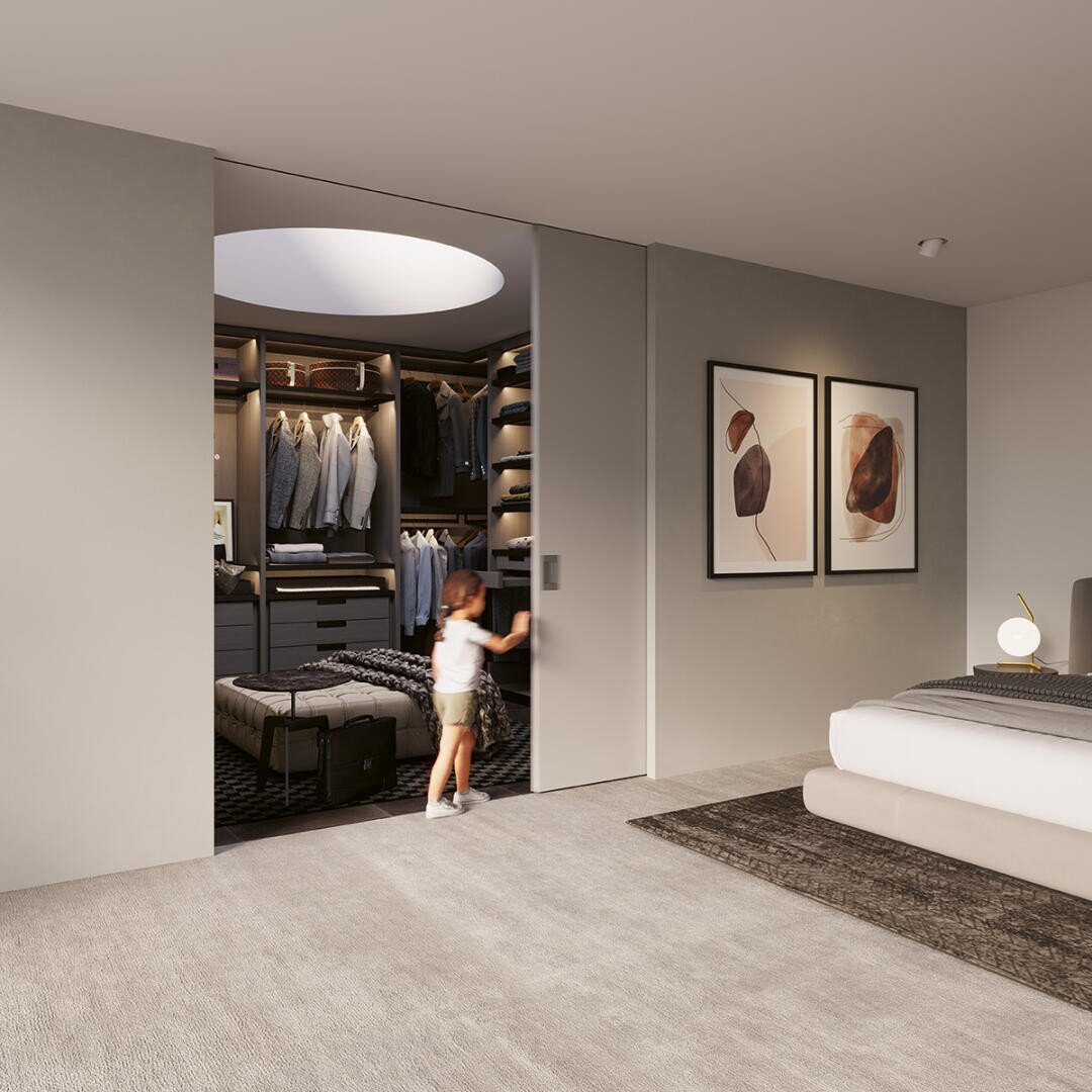 Ein kleines Kind öffnet eine Schiebetür zu einem modernen Ankleidezimmer mit Kleidung und Regalen, das mit einem aufgeräumten Schlafzimmer mit neutralem Dekor, einem Bett und gerahmten Kunstwerken an der Wand verbunden ist.