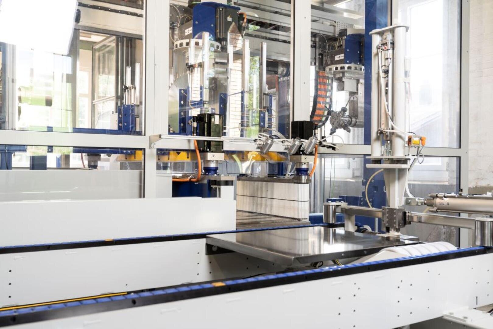 Machines modernes automatisées à l'intérieur d'une usine, comprenant des bras robotisés, des bandes transporteuses et des équipements en verre utilisés pour la fabrication industrielle ou les processus d'assemblage.