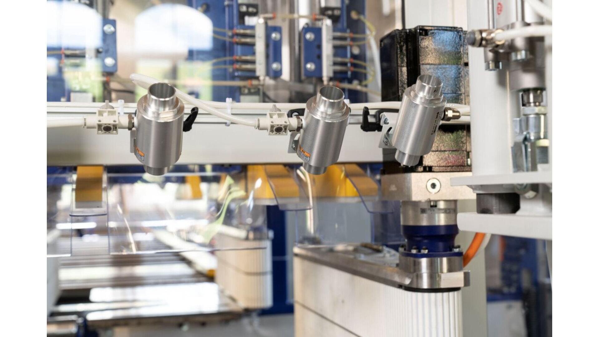 Gros plan d'une machine industrielle automatisée moderne dotée de bras robotisés, de capteurs et de câbles, travaillant avec des matériaux transparents dans un environnement de fabrication de haute technologie.