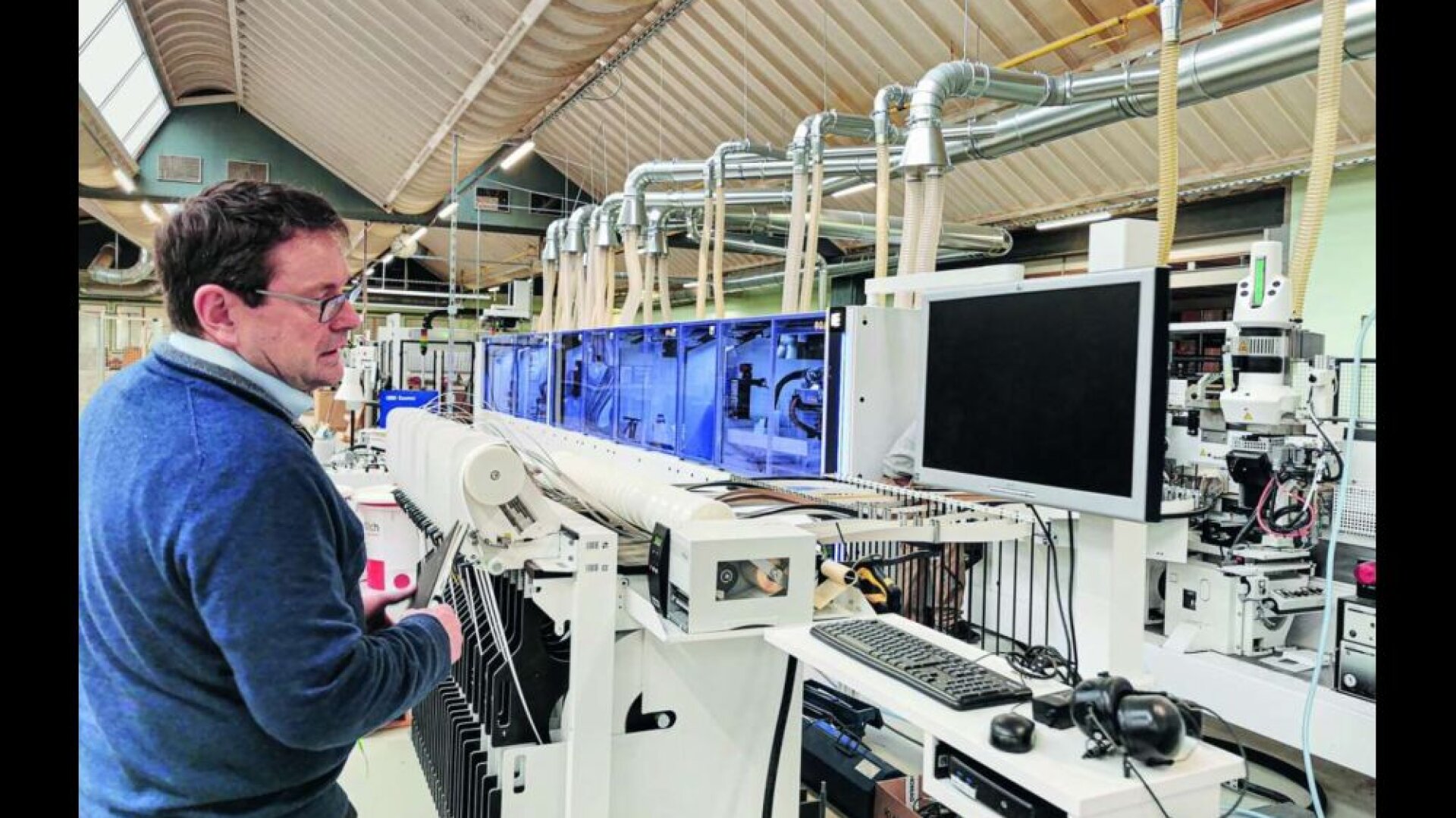 Ein Mann mit Brille steht in einer modernen Industrieanlage und bedient hochmoderne Maschinen mit Computermonitoren, Rohrleitungen und Geräten, die im gesamten Arbeitsbereich sichtbar sind.