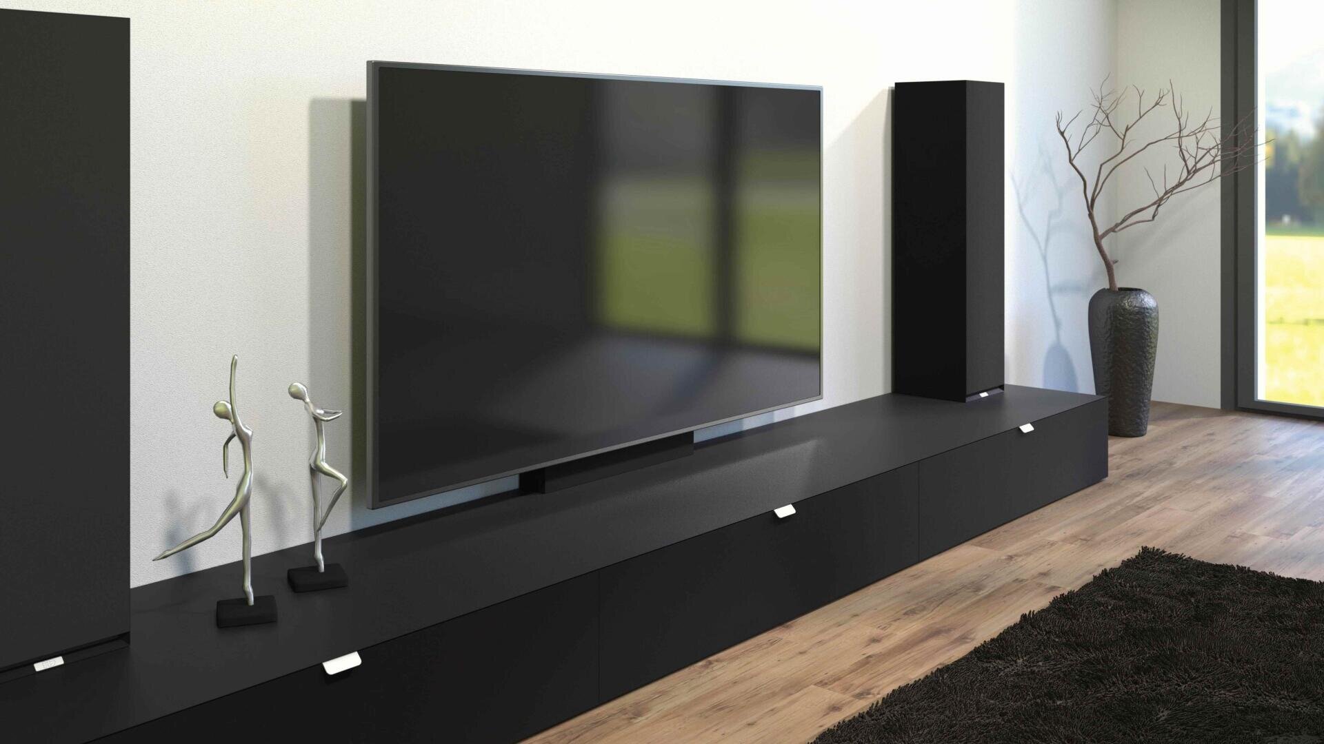 Ein modernes Wohnzimmer mit einem großen Flachbildfernseher auf einem schlichten schwarzen Schrank, zwei abstrakten silbernen Skulpturen, einem hohen schwarzen Lautsprecher und einer dekorativen Vase mit kahlen Zweigen an einem hellen Fenster.