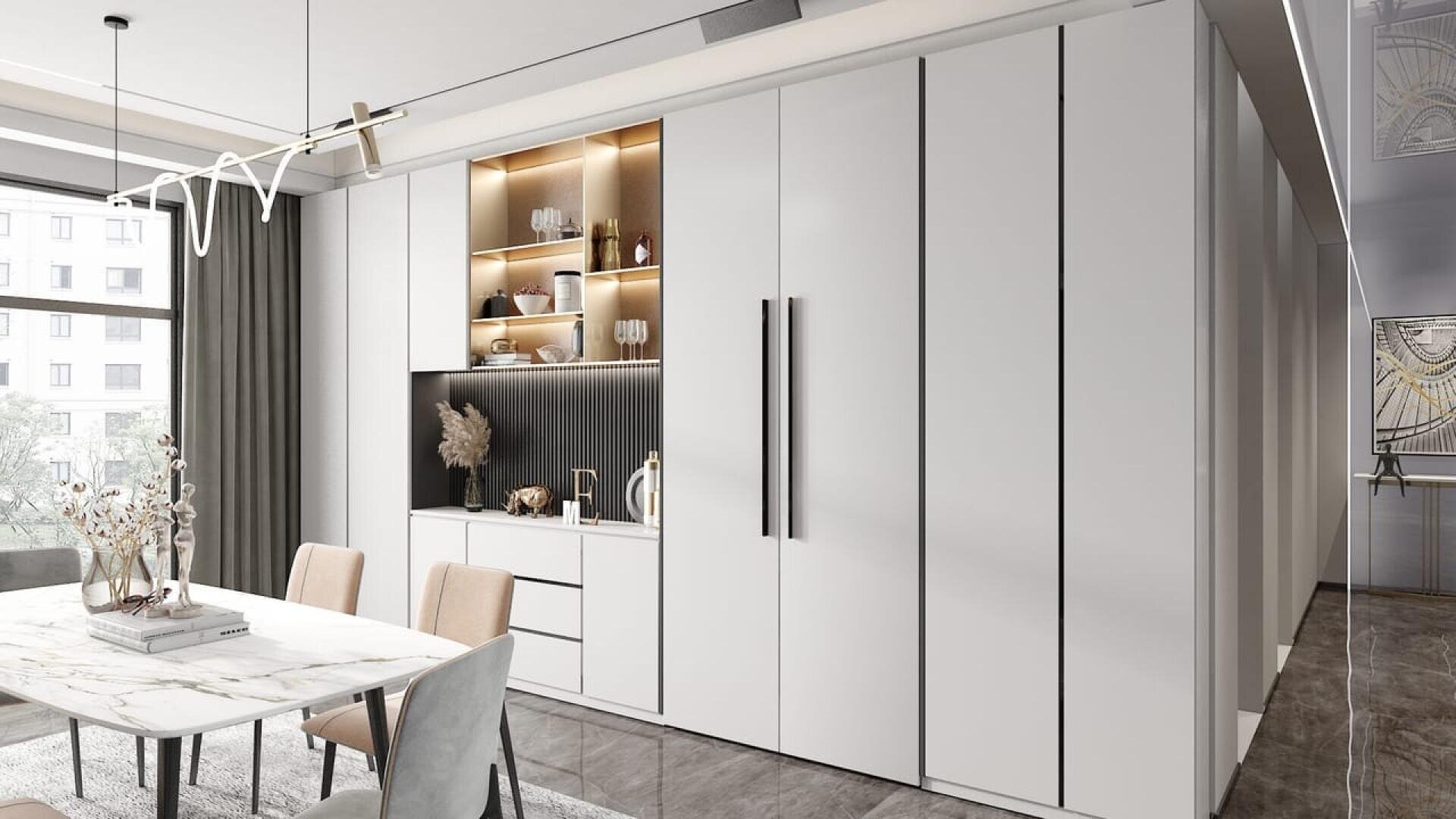 Une salle à manger moderne avec une table en marbre, des chaises beiges et un meuble blanc encastré avec des étagères ouvertes pour exposer la décoration. De grandes fenêtres laissent entrer la lumière naturelle et le sol est gris.