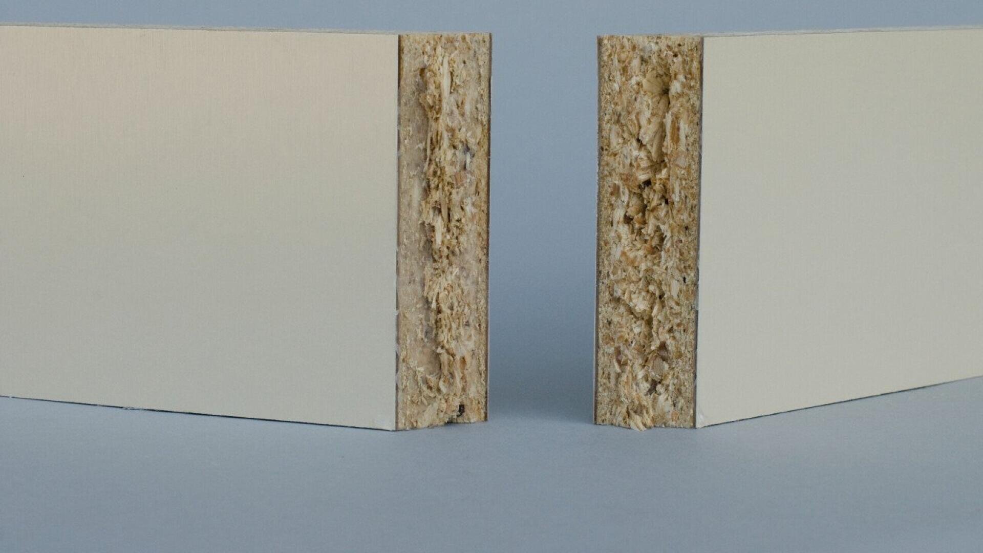 Deux morceaux rectangulaires de panneaux de particules avec des surfaces stratifiées de couleur claire, représentés debout avec des bords rugueux et texturés tournés vers l'avant sur un fond uni.