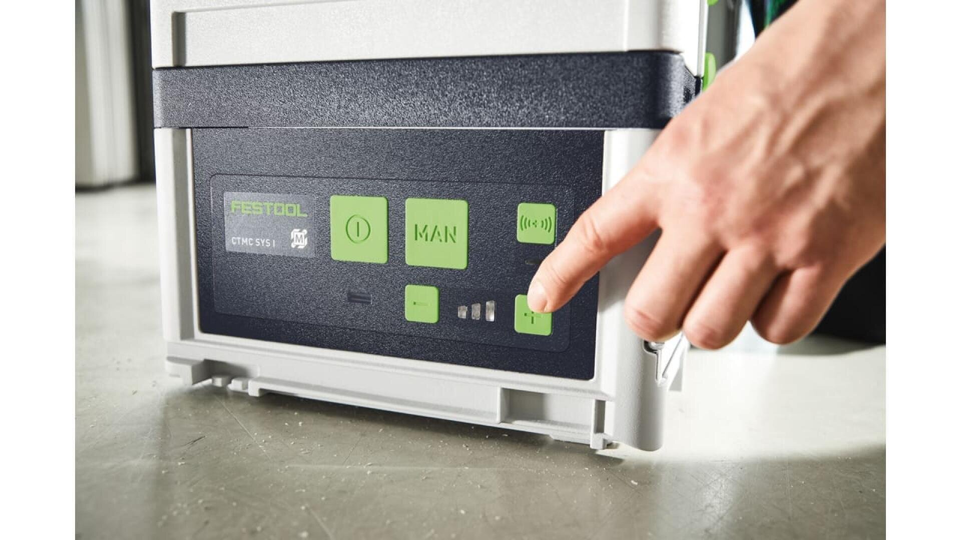 Gros plan d'une main appuyant sur un bouton vert sur le panneau de commande d'un dépoussiéreur Festool CTM MIDI, avec d'autres boutons étiquetés et des voyants lumineux visibles.
