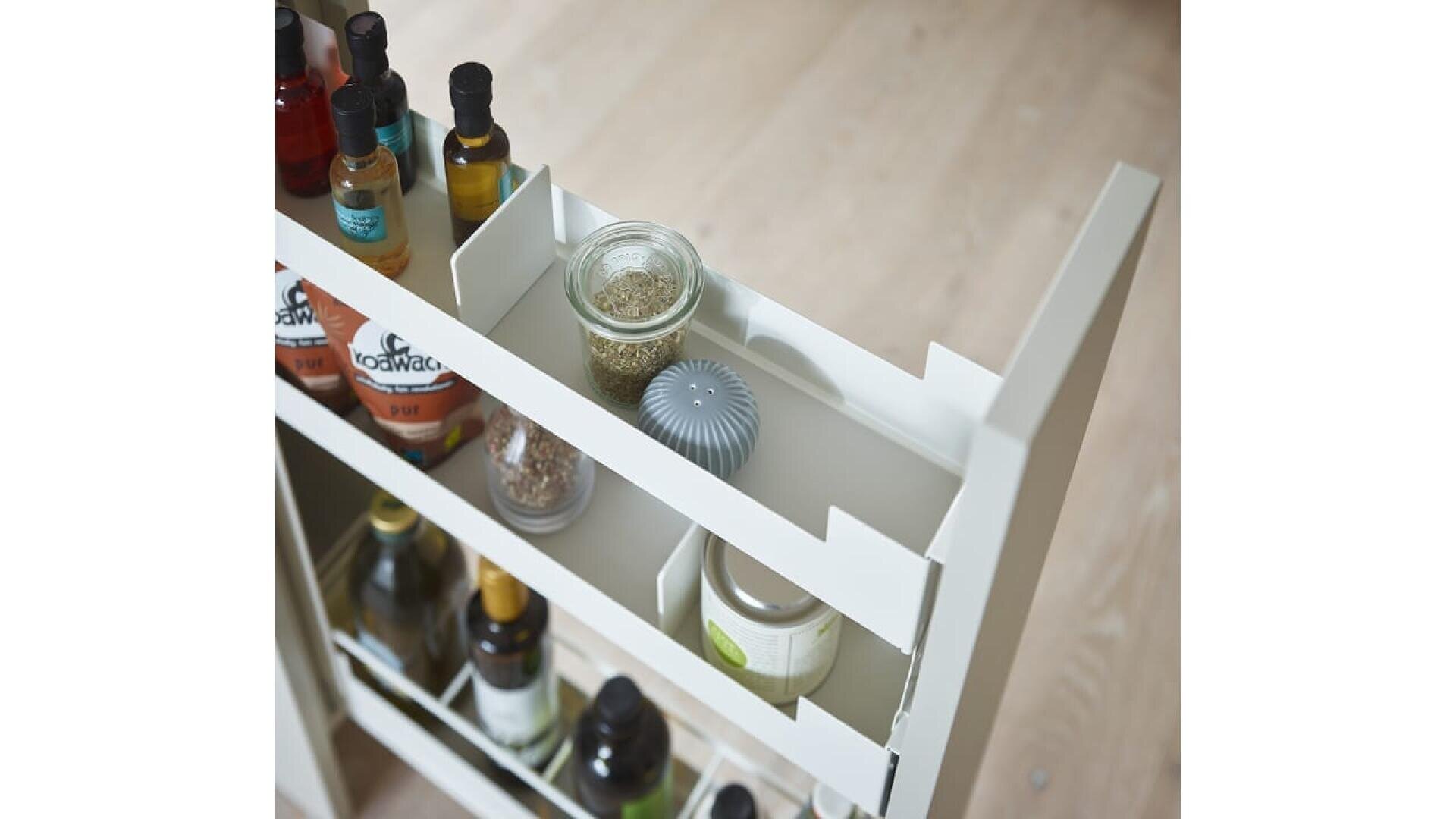 Gros plan sur l'étagère d'un meuble de cuisine blanc coulissant, contenant des bouteilles d'huile, de vinaigre, des bocaux d'épices et un petit récipient, sur un sol en bois clair.