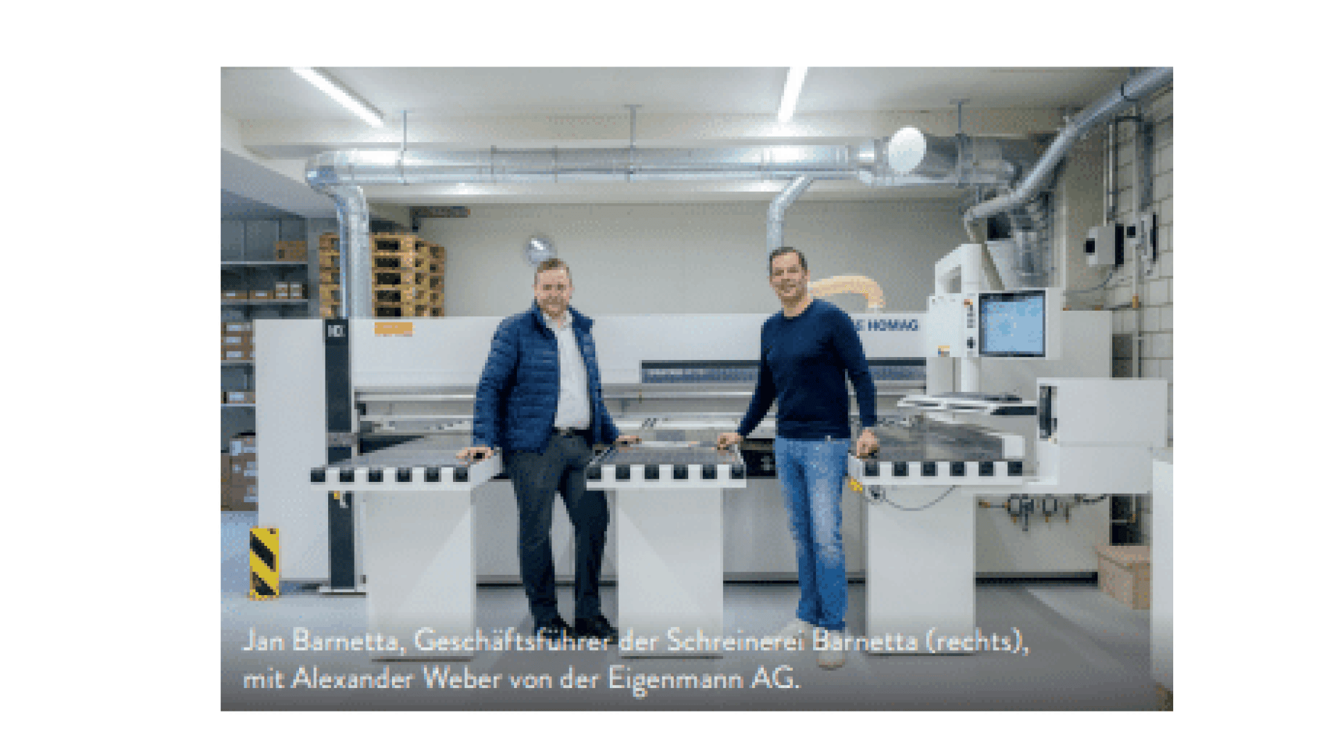 Zwei Männer stehen vor einer großen Industriemaschine in einer Werkstatt mit Metallrohren, Regalen und Kisten. Beide lächeln; der eine trägt eine Jacke, der andere einen Pullover. Eine Bildunterschrift identifiziert sie und ihre Unternehmen.