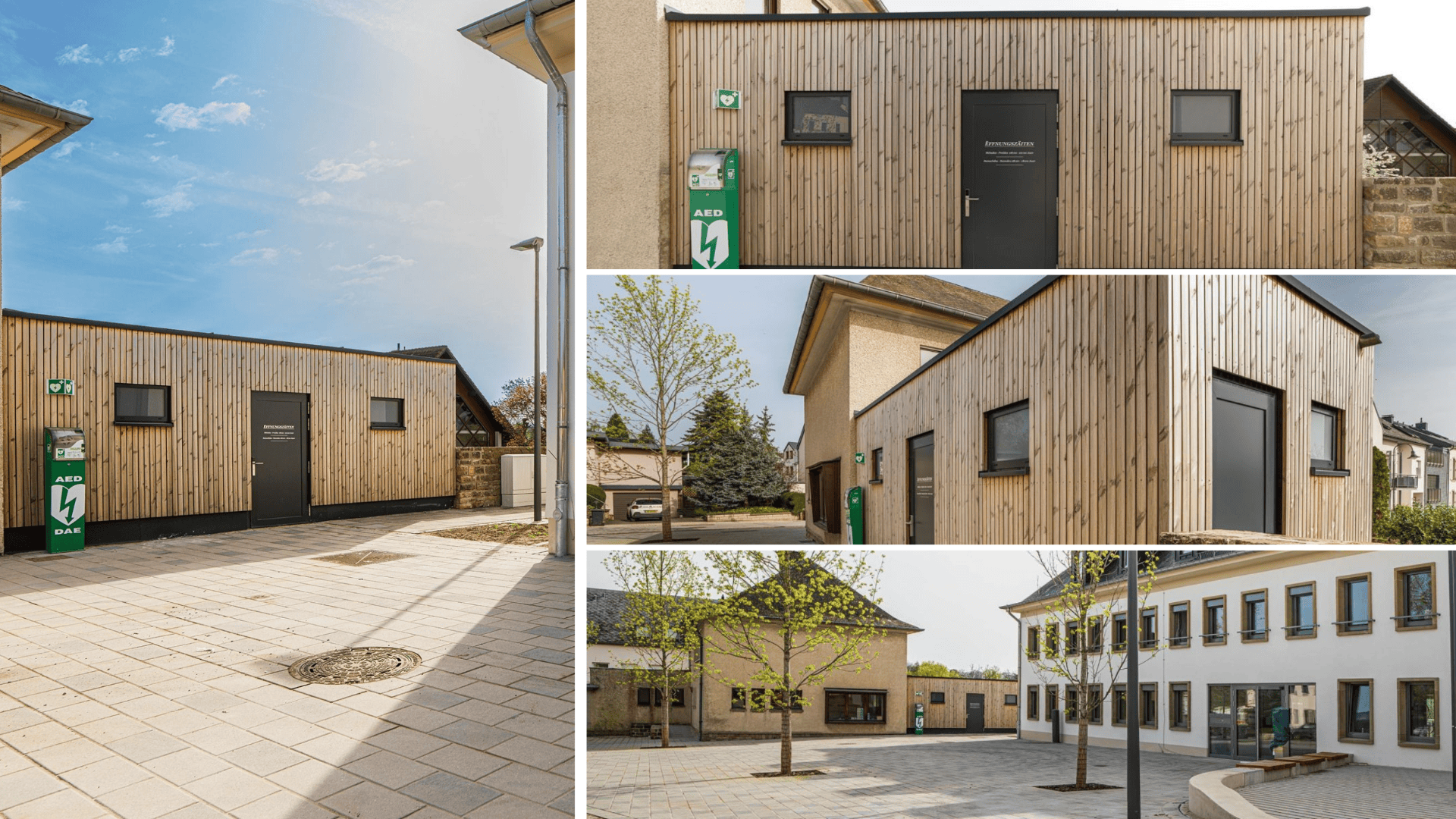 Ein kleines, modernes Gebäude mit Holzverkleidung steht in einem gepflasterten Hof, umgeben von älteren Gebäuden. An der Außenwand in der Nähe des Eingangs ist ein AED-Defibrillatorkasten angebracht. Bäume und klarer Himmel sind zu sehen.