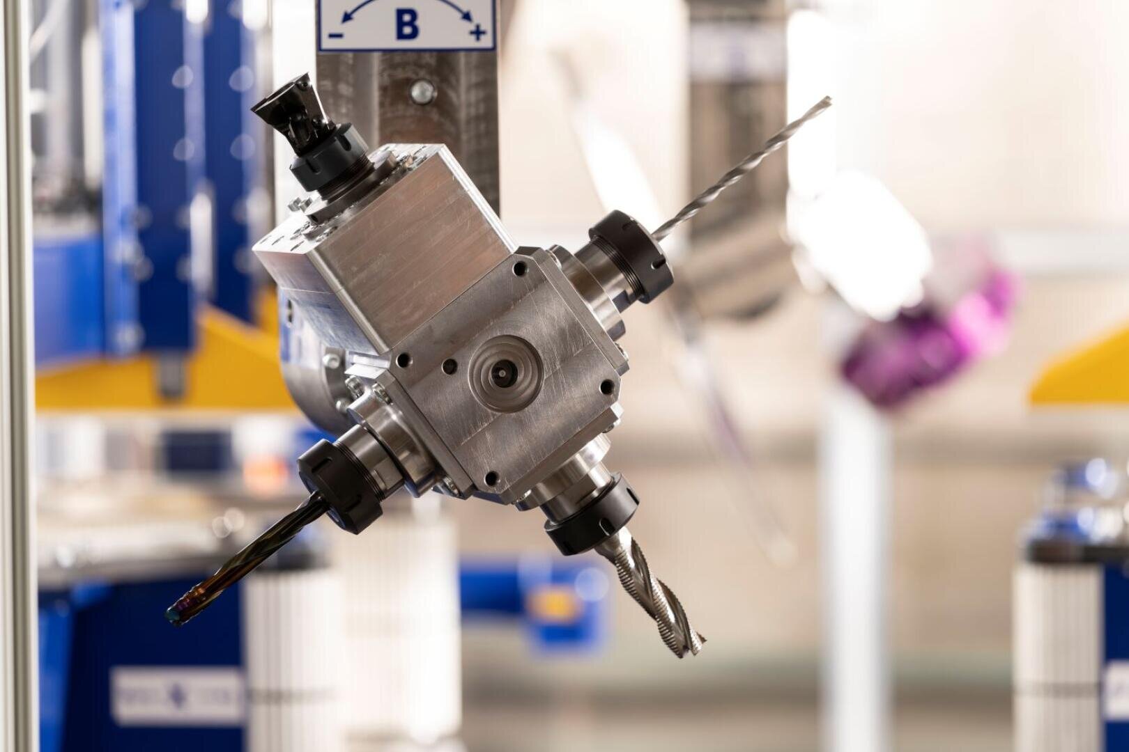 Nahaufnahme eines metallischen Industrieroboters mit angebrachten Bohrern, der an einer Maschine in einer hellen, modernen Fertigungsumgebung montiert ist.