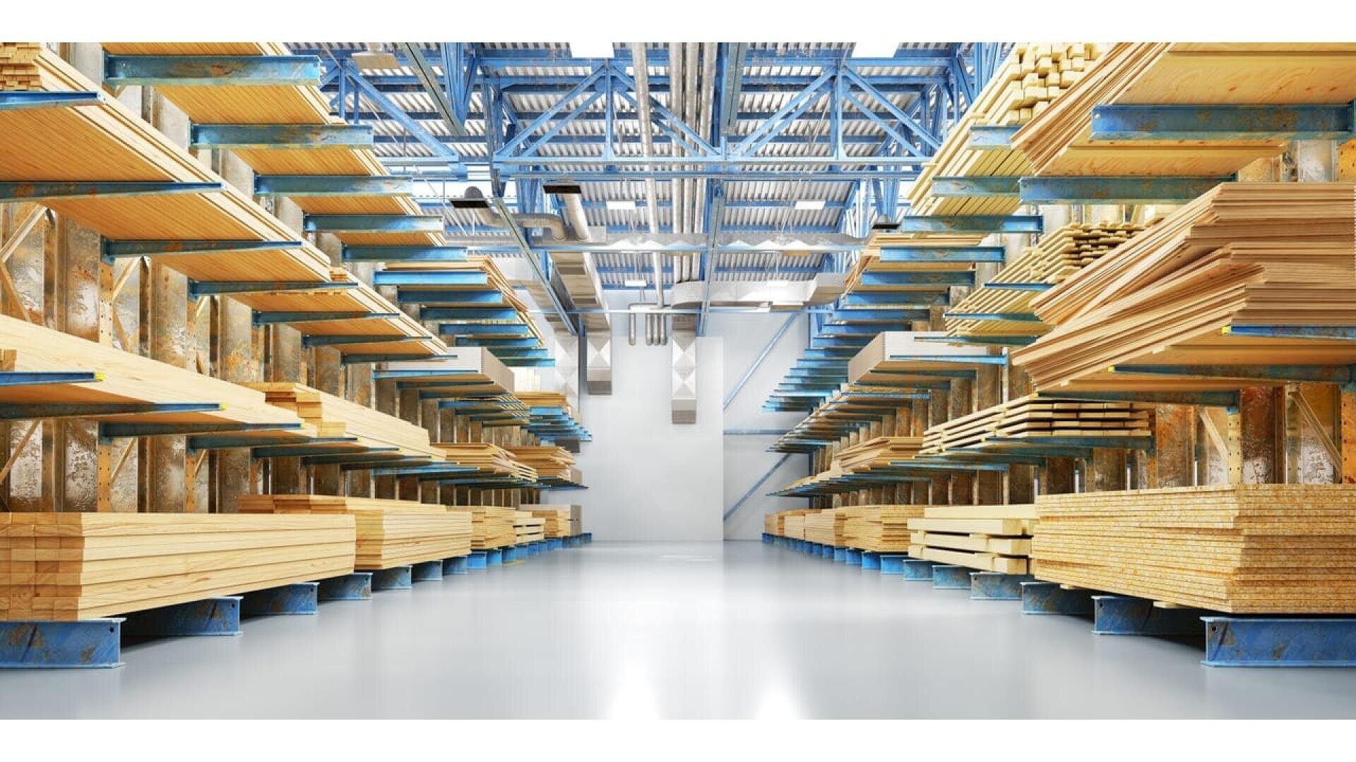 Des piles de planches bien rangées sont stockées sur des étagères métalliques à l'intérieur d'un grand entrepôt bien éclairé, avec de hauts plafonds et un sol en béton brillant.