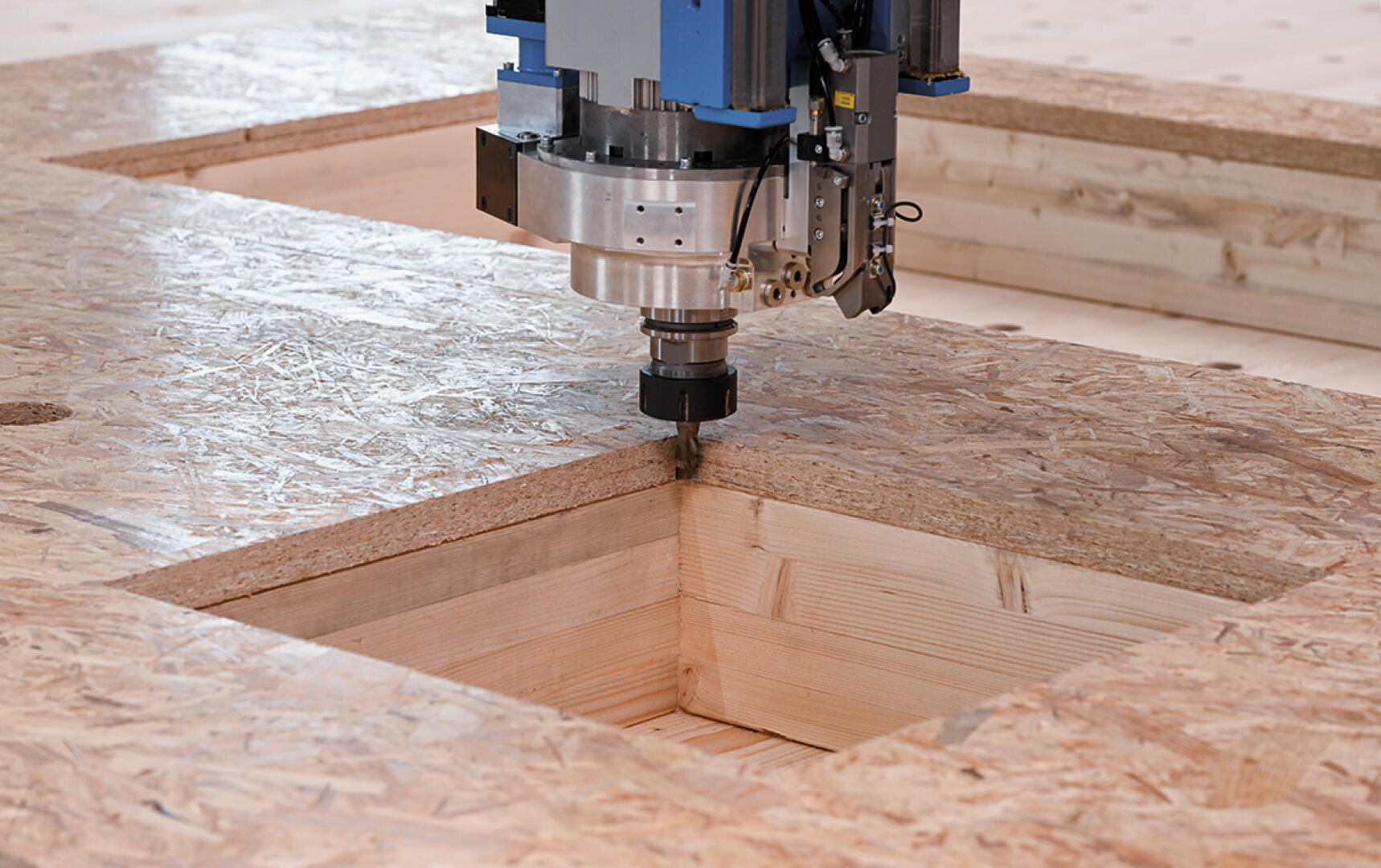 Eine CNC-Maschine schneidet präzise ein quadratisches Loch in eine OSB-Platte (Oriented Strand Board) und eine Holzplatte und zeigt so die automatisierte Holzbearbeitung.