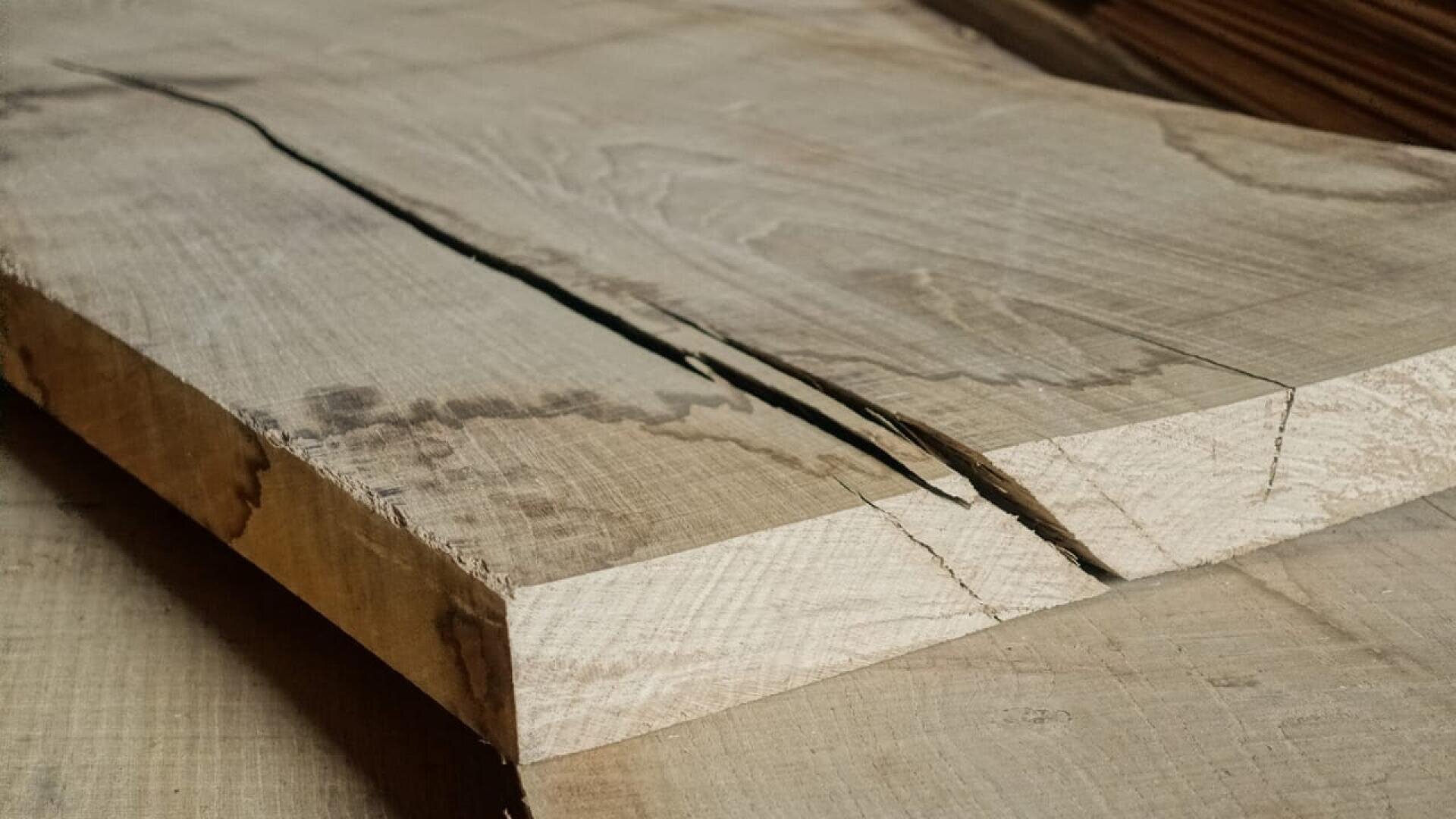 Vue rapprochée d'une planche de bois clair avec une grande fissure dentelée au centre, montrant des surfaces rugueuses et irrégulières.