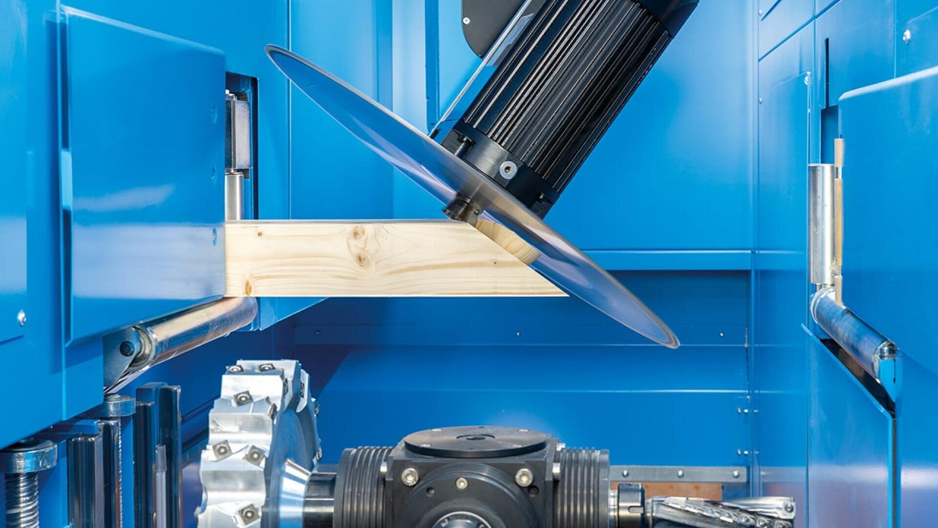 Eine Kreissäge mit einem großen Metallblatt schneidet durch eine Holzplatte in einer blauen Industriemaschine. Um den Schnittbereich herum sind verschiedene mechanische Komponenten und Metallteile zu sehen.