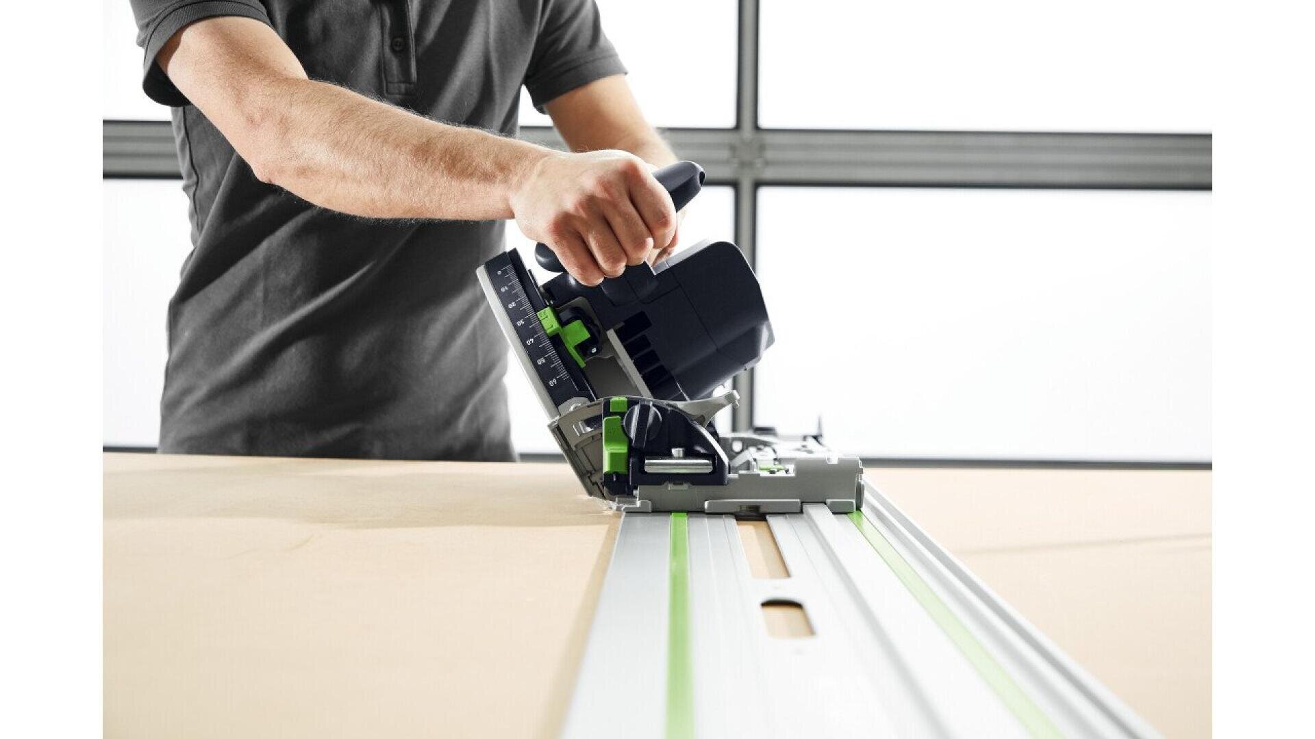 Une personne utilise une scie circulaire avec un rail de guidage pour couper une feuille de bois sur un établi. L'accent est mis sur l'outil et les mains, le corps étant partiellement visible.