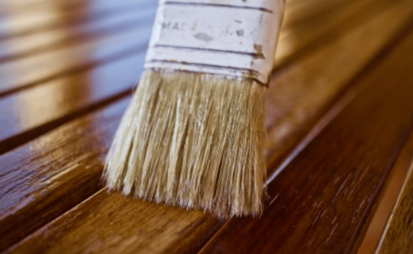 Nahaufnahme eines Pinsels, der eine glänzende Lasur auf Holzlatten aufträgt, wobei die feuchte, glänzende Oberfläche neben dem trockenen Holz hervorgehoben wird.