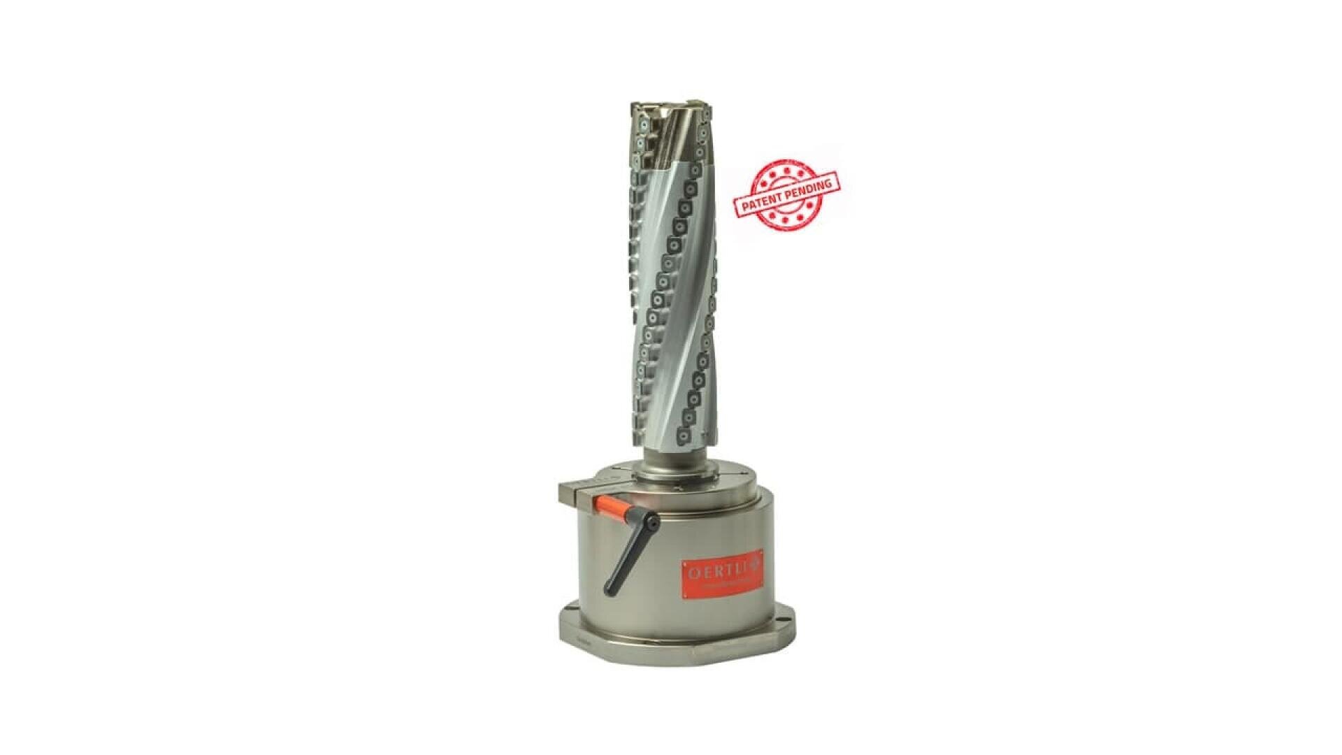 Un dispositif mécanique cylindrique métallique avec un motif en spirale et un levier sur sa base. L'appareil porte une étiquette orange et un timbre "Patent Pending" (brevet en cours d'homologation) est visible à l'arrière-plan.