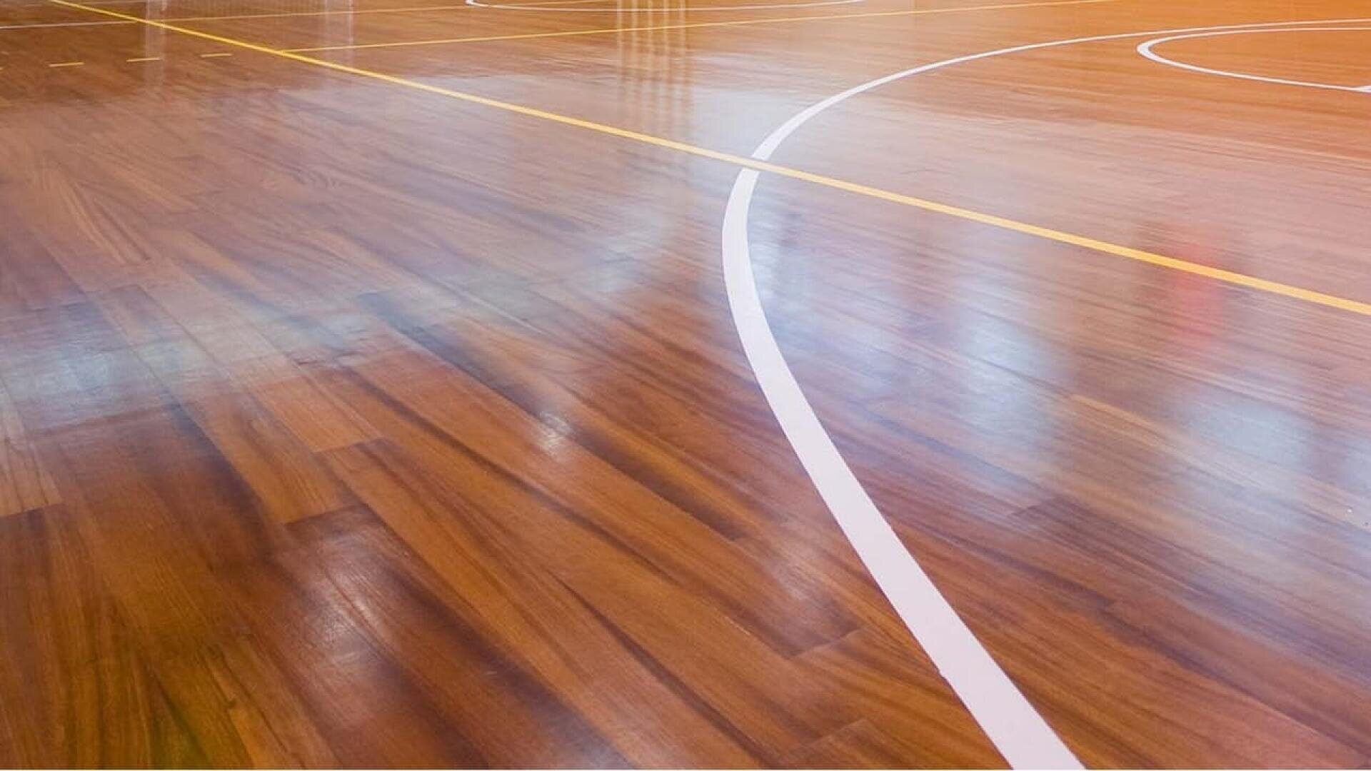 Terrain de sport d'intérieur en bois brillant avec des lignes blanches et jaunes marquant les limites, vu sous un angle sans joueurs ni équipements visibles.