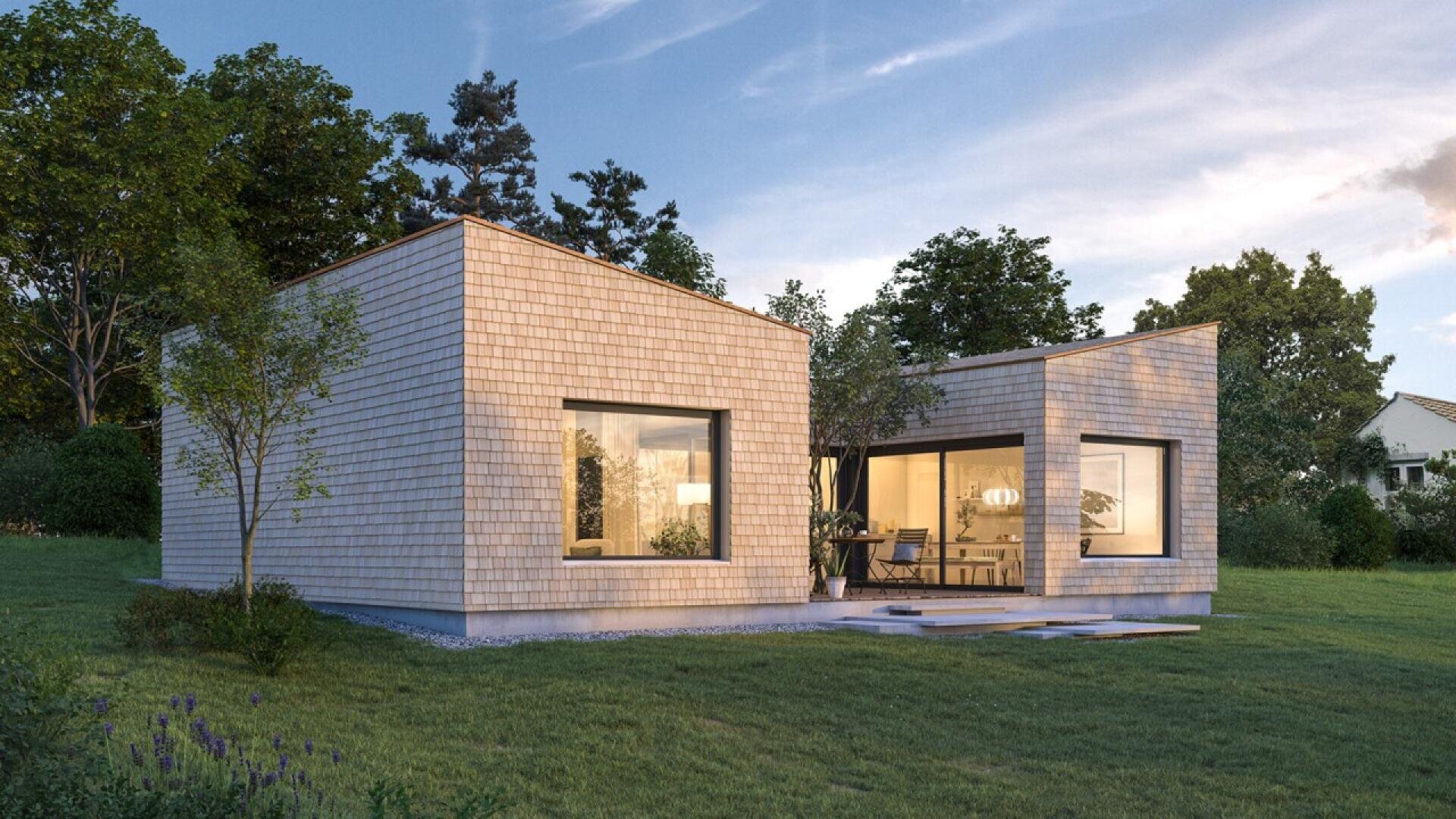 Une maison moderne de plain-pied avec des bardeaux de bois de couleur claire, de grandes fenêtres et des toits plats, entourée d'herbe et d'arbres dans un cadre suburbain au coucher du soleil.
