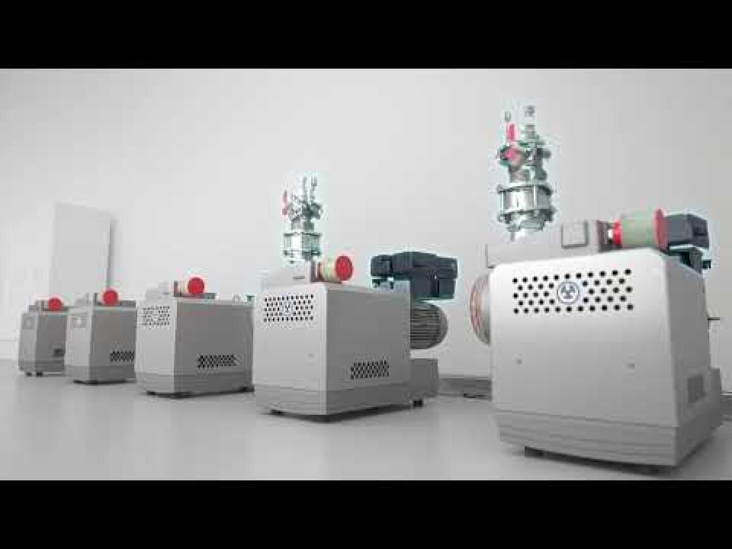 Eine Reihe industrieller Vakuumpumpen, silberfarben mit roten und blauen Akzenten, ist auf einem sauberen weißen Boden vor einer schlichten weißen Wand in einem gut beleuchteten Raum aufgereiht.