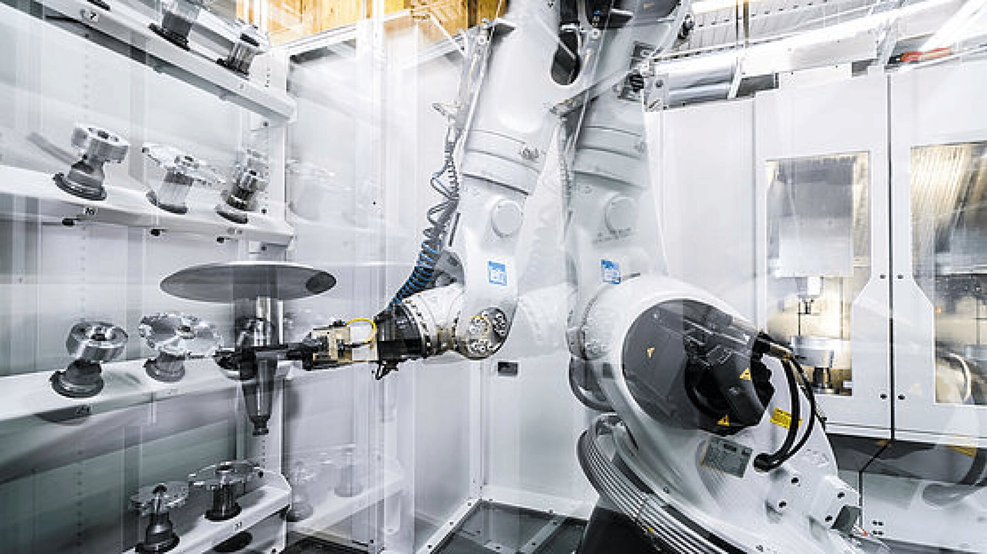Ein Roboterarm operiert im Inneren einer automatisierten Hightech-Industrieanlage, die von Regalen mit verschiedenen Maschinenteilen und Metallwerkzeugen umgeben ist. Die Umgebung wirkt sauber und modern, wobei der Schwerpunkt auf fortschrittlicher Fertigungstechnologie liegt.
