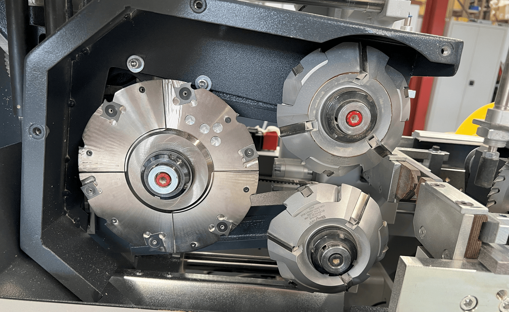 Gros plan sur trois grandes têtes de coupe ou de fraisage de métaux à l'intérieur d'une machine industrielle. Les pièces de la machine sont brillantes et métalliques, avec des boulons visibles, sur un fond gris foncé et argenté.