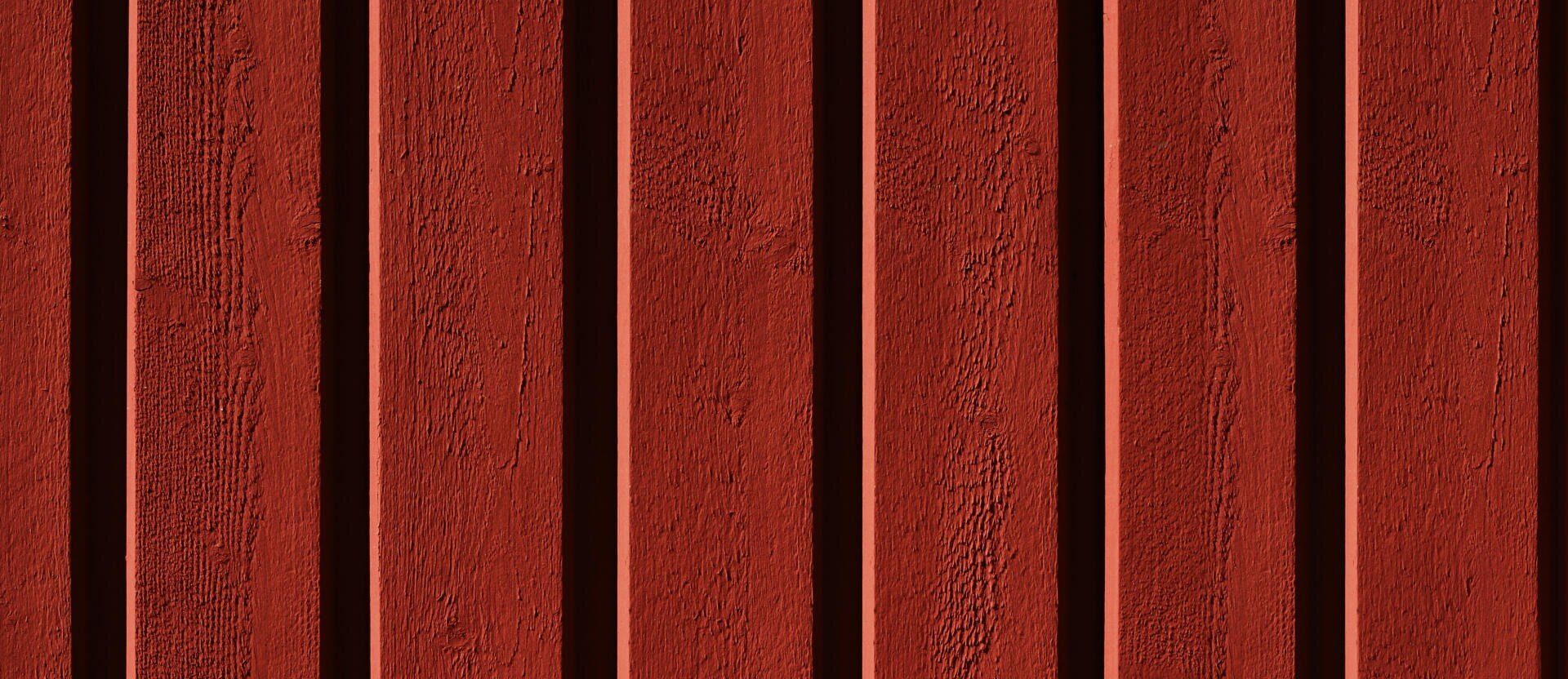 Planches verticales en bois rouge, uniformément réparties, avec une surface structurée et une alternance de sections en relief et en creux, formant un motif rayé.