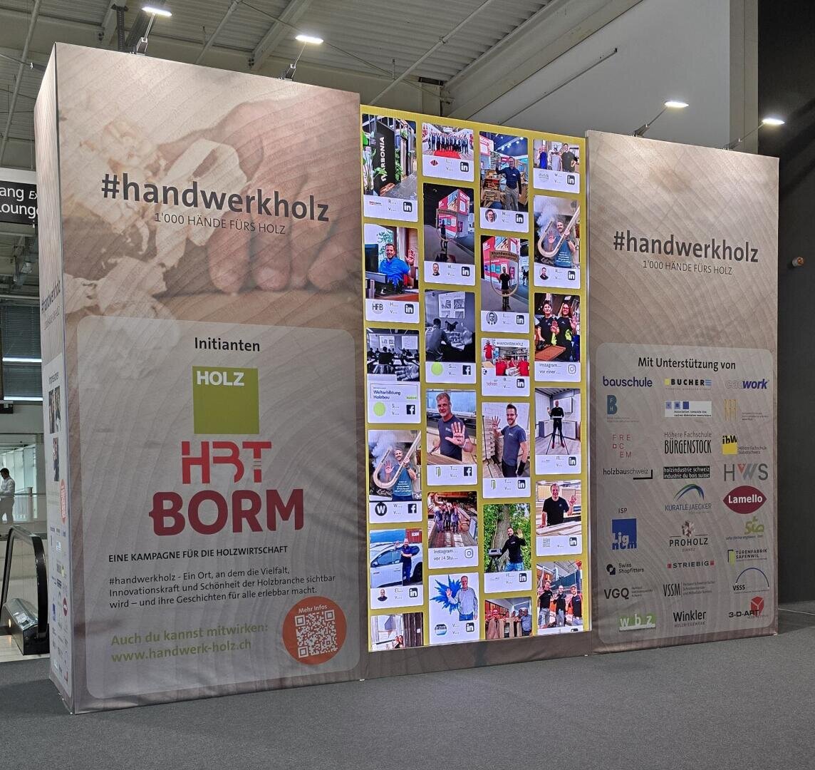 Auf einem großen Ausstellungsdisplay sind der Hashtag #handwerkholz, Kampagnenlogos, Partnersponsoren und eine Collage von Social-Media-Beiträgen zum Thema Holzbearbeitung zu sehen, mit QR-Codes und Informationstafeln auf beiden Seiten.