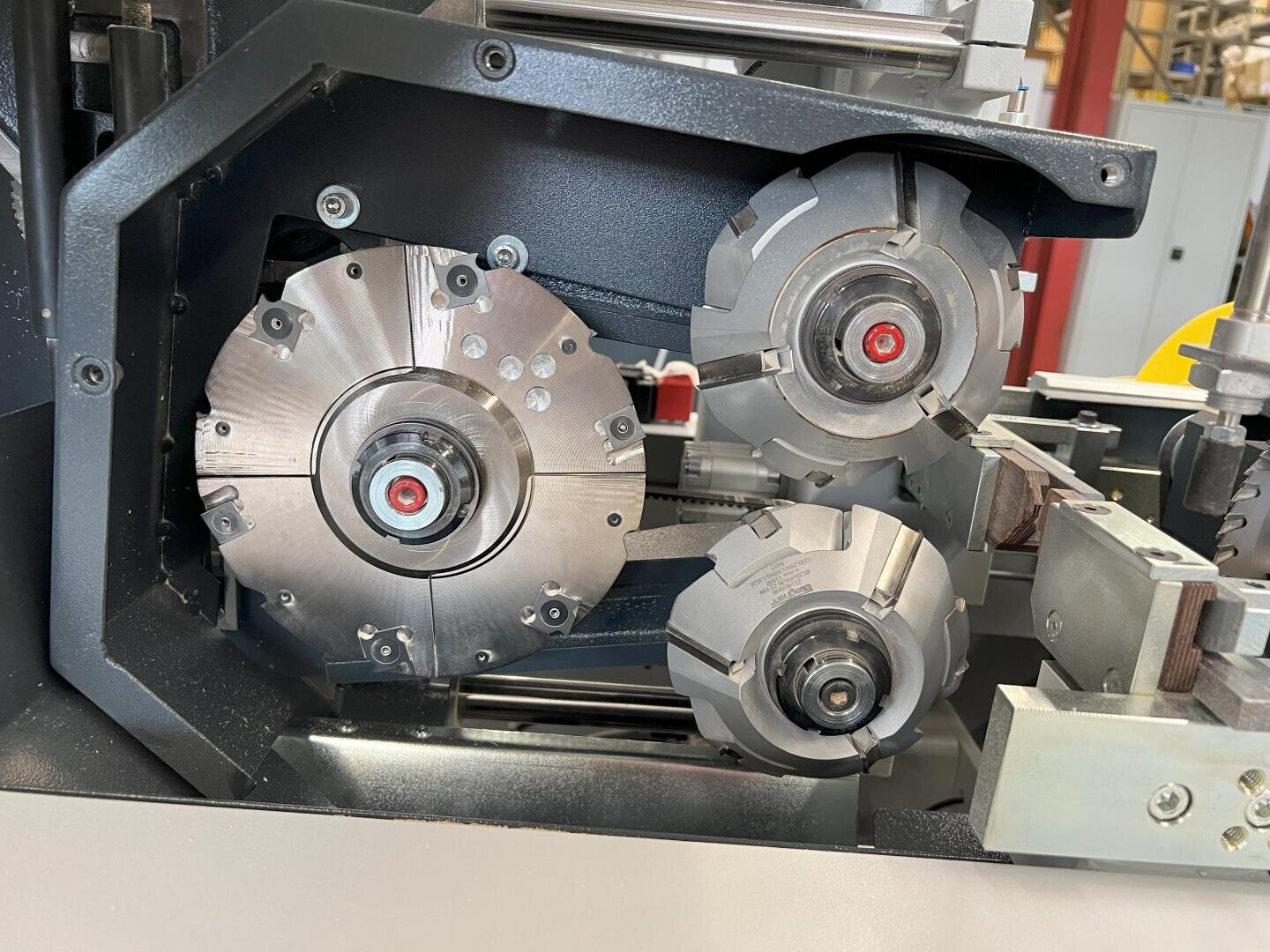 Nahaufnahme von drei Metallschneid- oder Formgebungsscheiben in einer Industriemaschine, die scharfe Kanten, Bolzen und mechanische Komponenten mit einer metallischen Oberfläche und einige sichtbare Maschinenteile im Hintergrund zeigt.