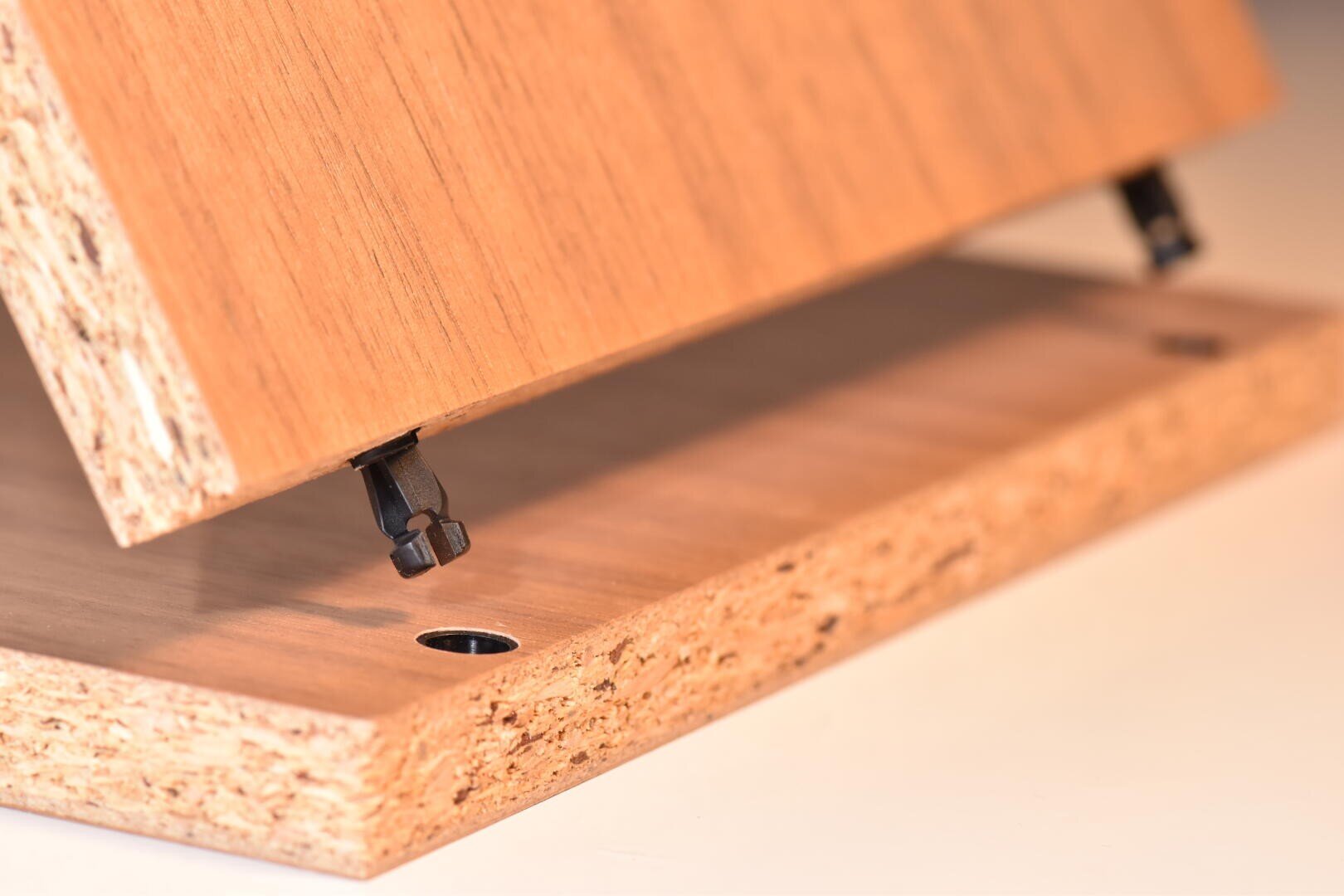 Nahaufnahme von zwei Spanplatten, die mit Nockenverschlüssen montiert werden, wobei der Verriegelungsmechanismus teilweise zwischen den Platten eingesetzt ist.