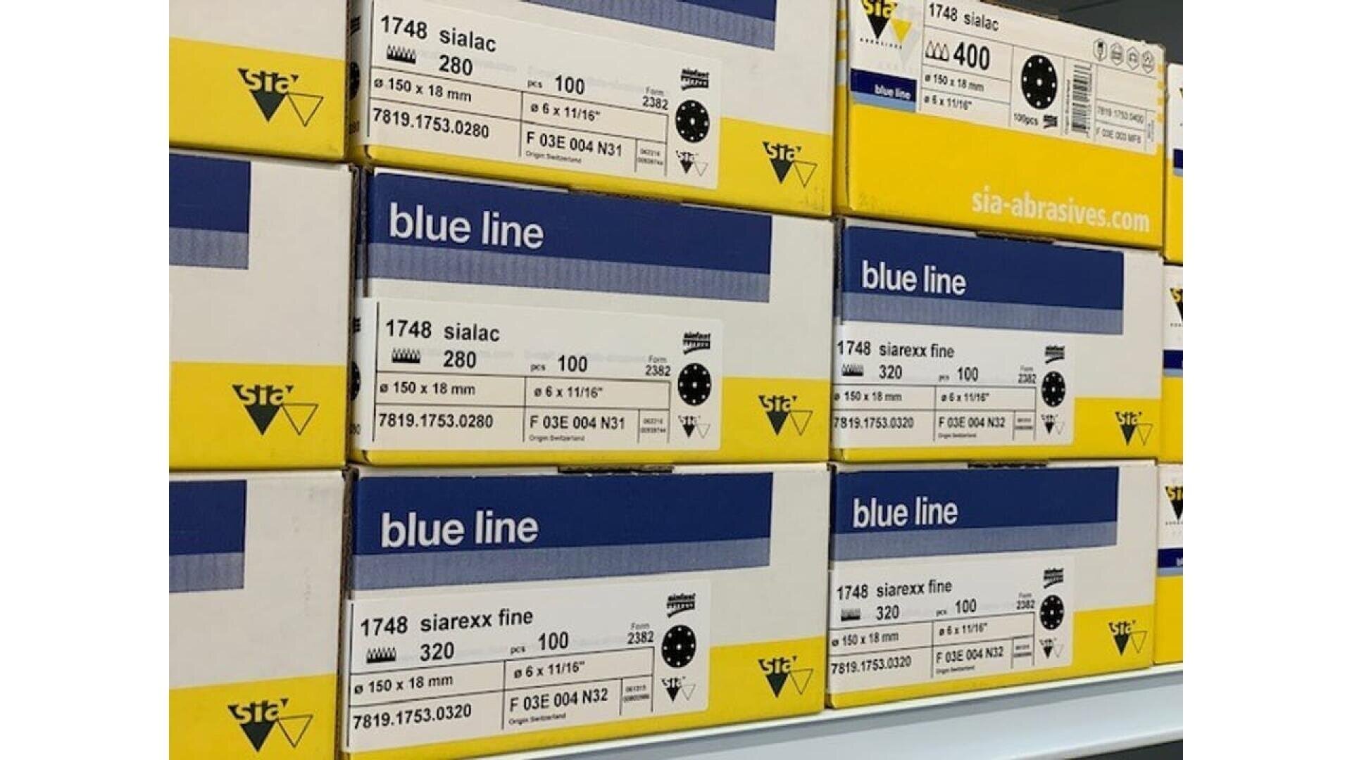Boîtes empilées d'abrasifs Sia blue line de différents grains, y compris sialac 280, 400, et siarex fine 320, avec des étiquettes jaunes et bleues sur une étagère.