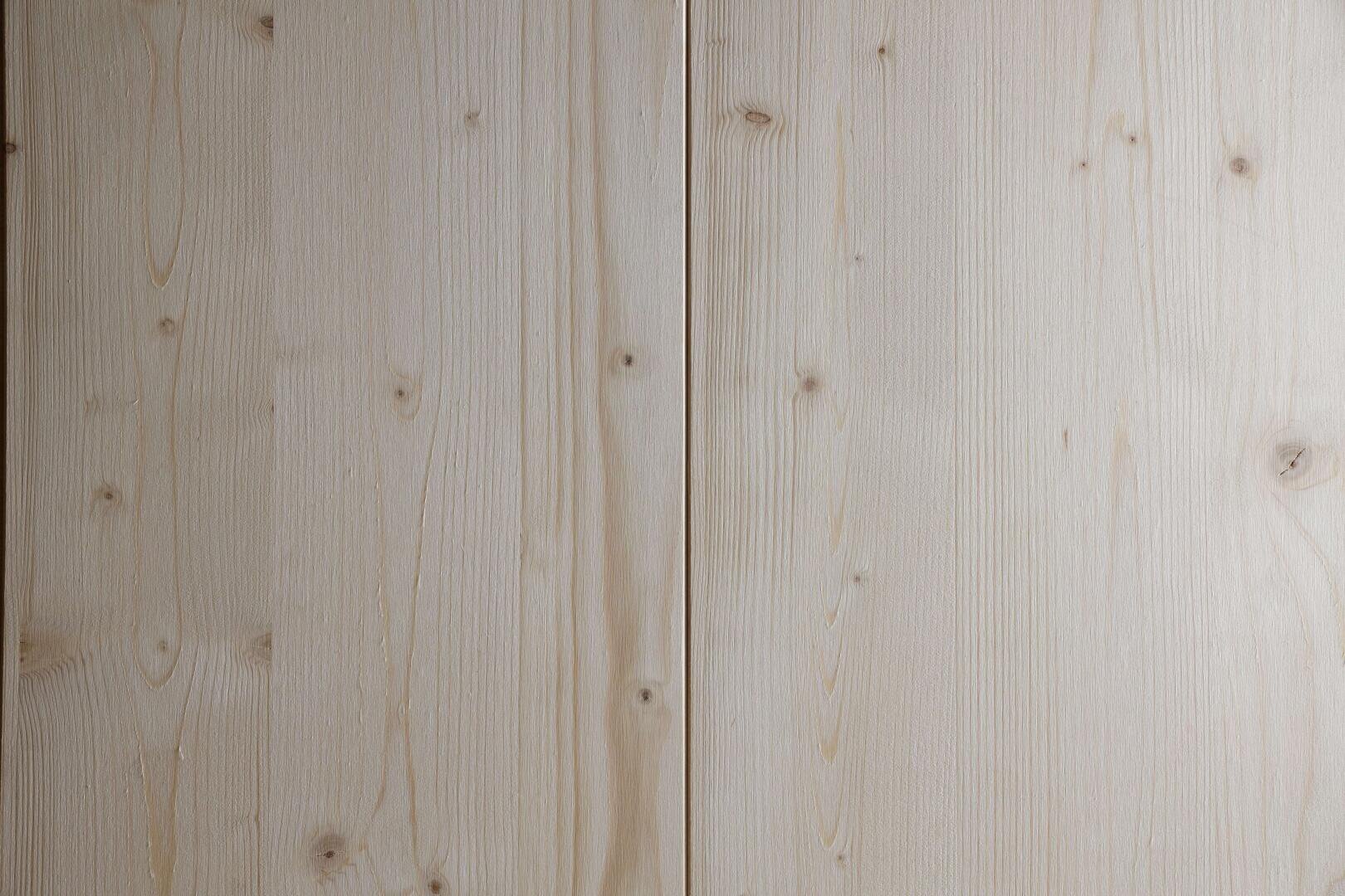Nahaufnahme von zwei hellen Holzbrettern, deren natürliche Maserung und kleine Äste sichtbar sind, die nebeneinander liegen und durch einen schmalen Spalt voneinander getrennt sind.