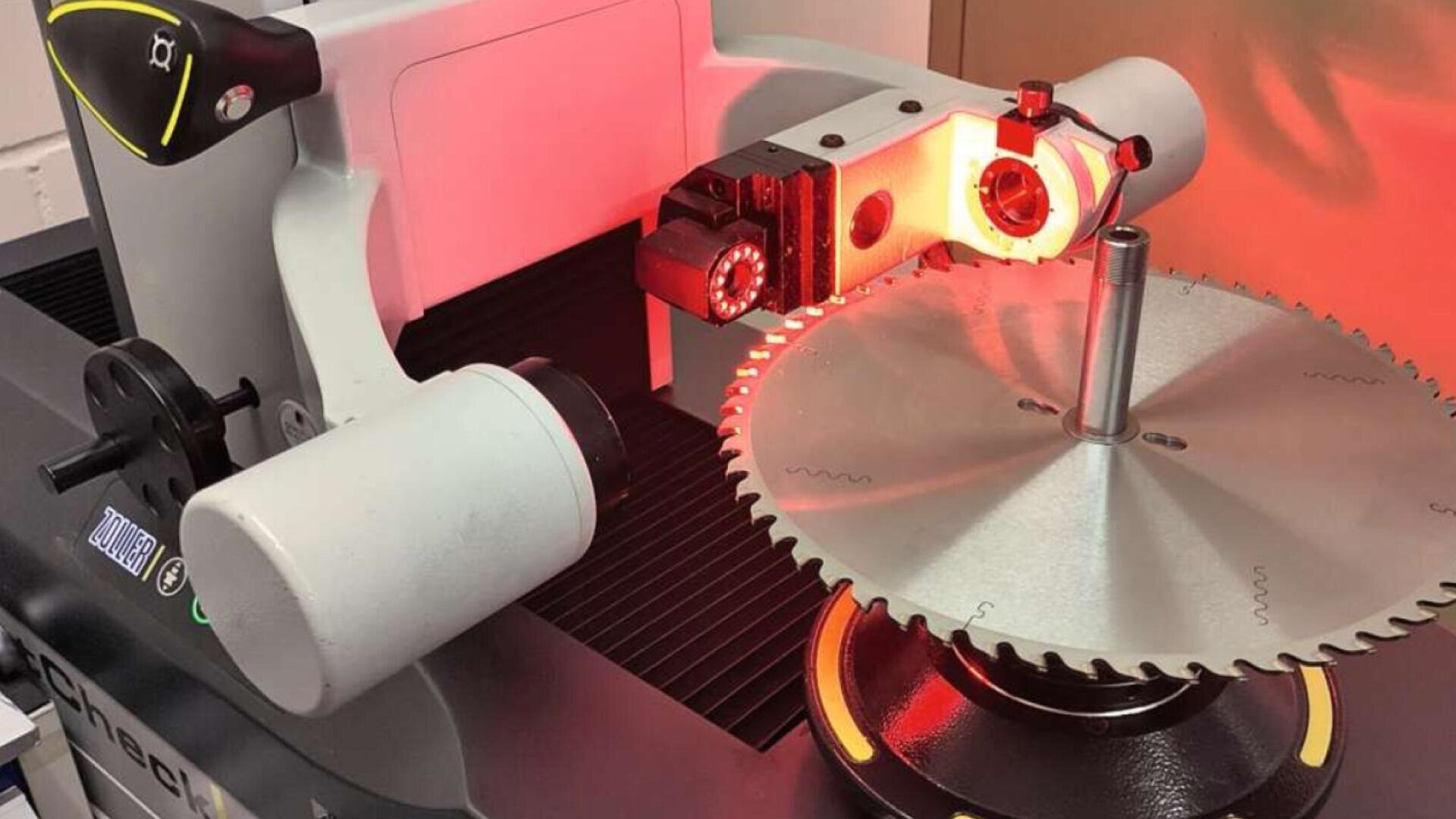 Nahaufnahme eines Kreissägeblatts, das von einer optischen Hightech-Messmaschine mit rotem Laserlicht geprüft wird.
