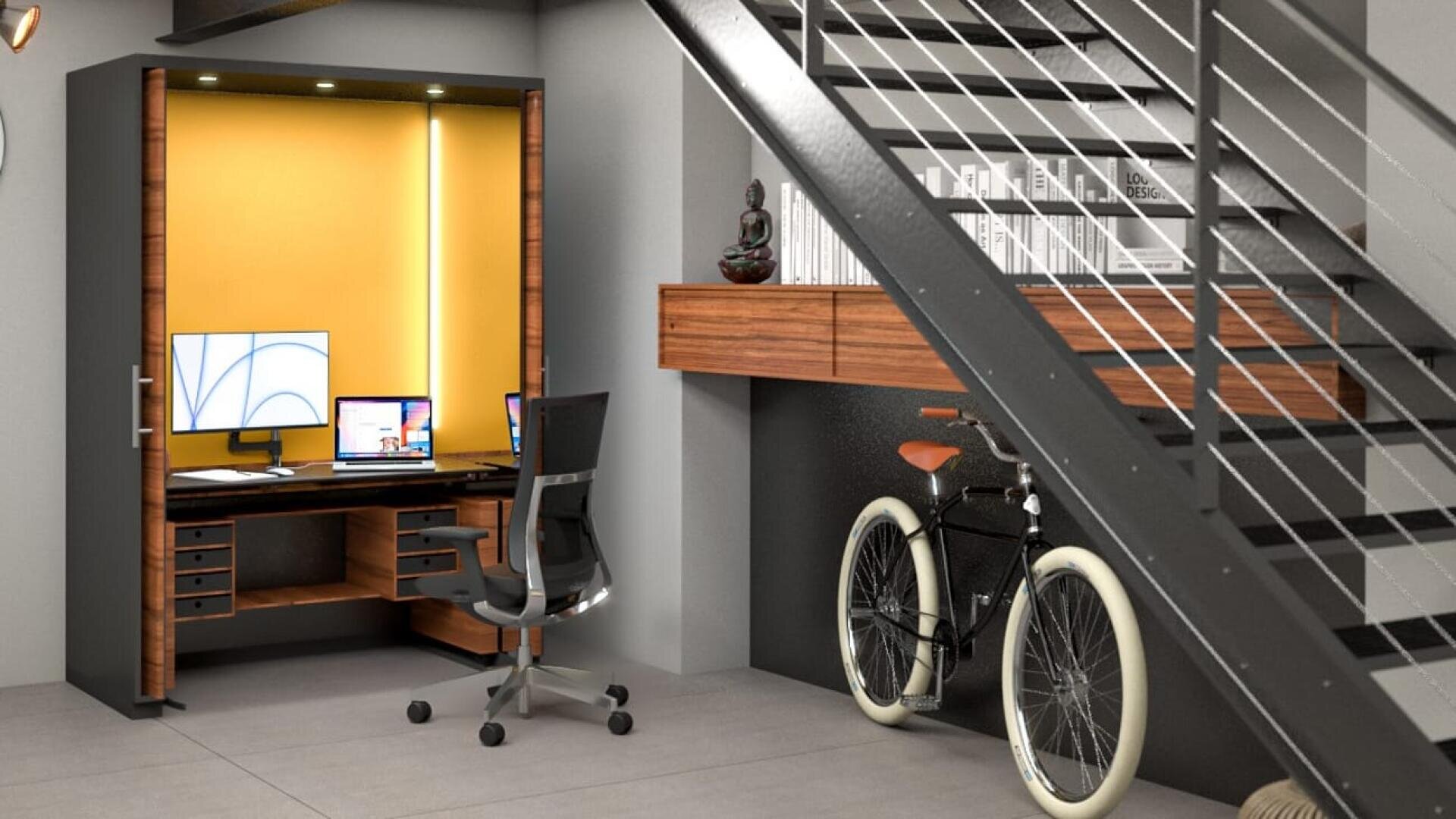 Modernes Heimbüro unter einer Treppe mit einem Schreibtisch, einem Stuhl, zwei Monitoren, Bücherregalen, einem Fahrrad und dekorativen Gegenständen, darunter eine Buddha-Statue und Bücher, vor einer gelben Akzentwand und einem grauen Bodenbelag.