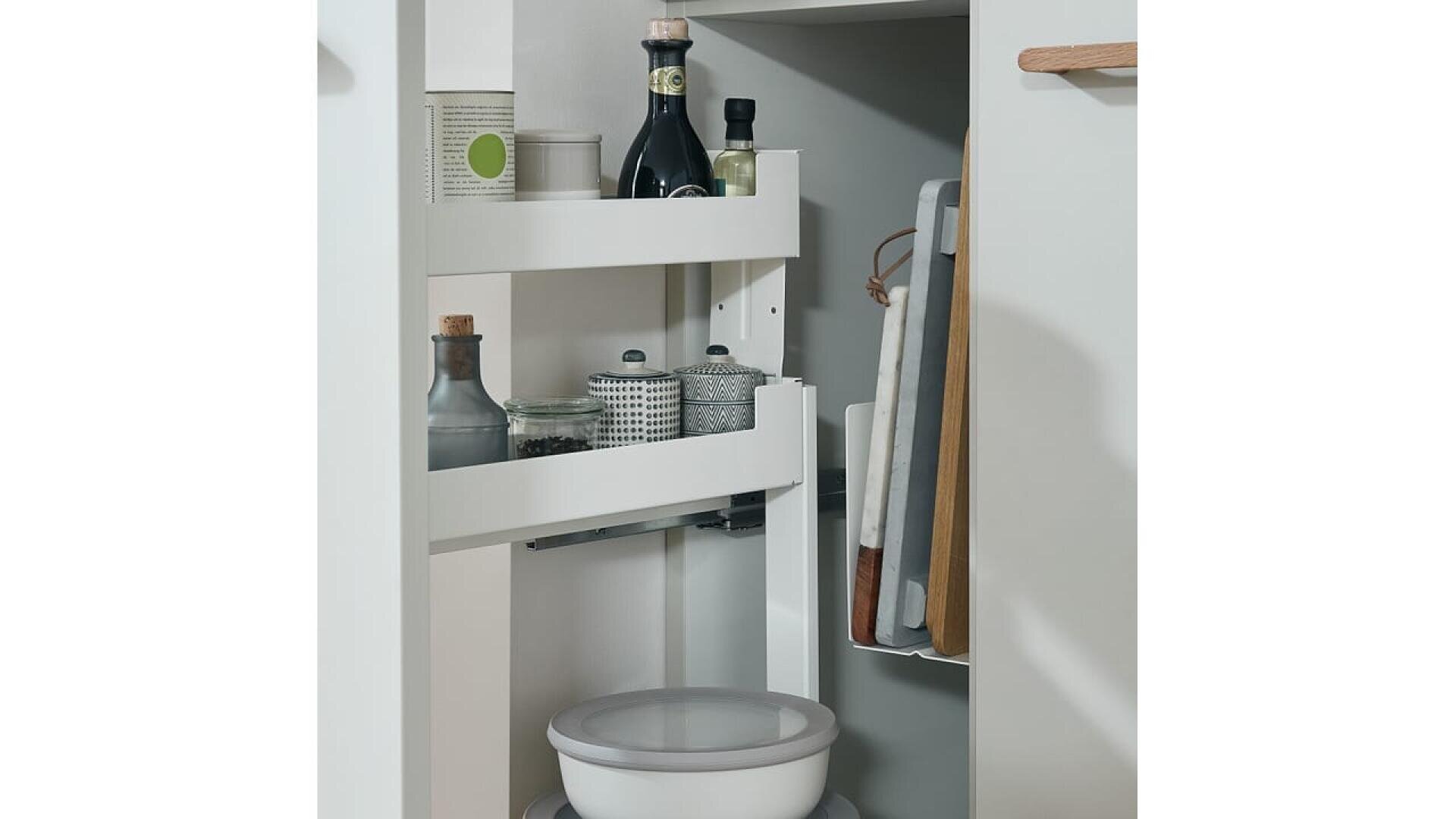 Un meuble de cuisine blanc avec une étagère coulissante contenant des bouteilles, des bocaux et des récipients. Plusieurs planches à découper sont rangées verticalement sur la porte, et un récipient de cuisine rond se trouve en bas.