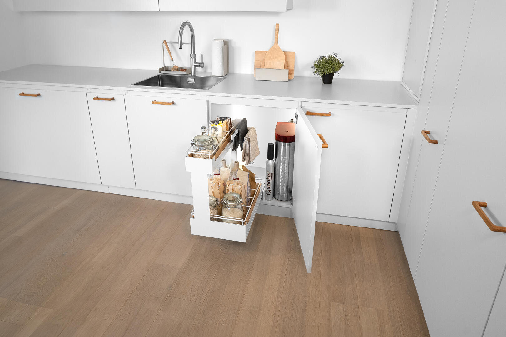 Eine moderne weiße Küche mit Holzgriffen und einem ausziehbaren Schrank mit Gläsern, Flaschen und Utensilien neben einem Wasseraufbereitungsgerät.