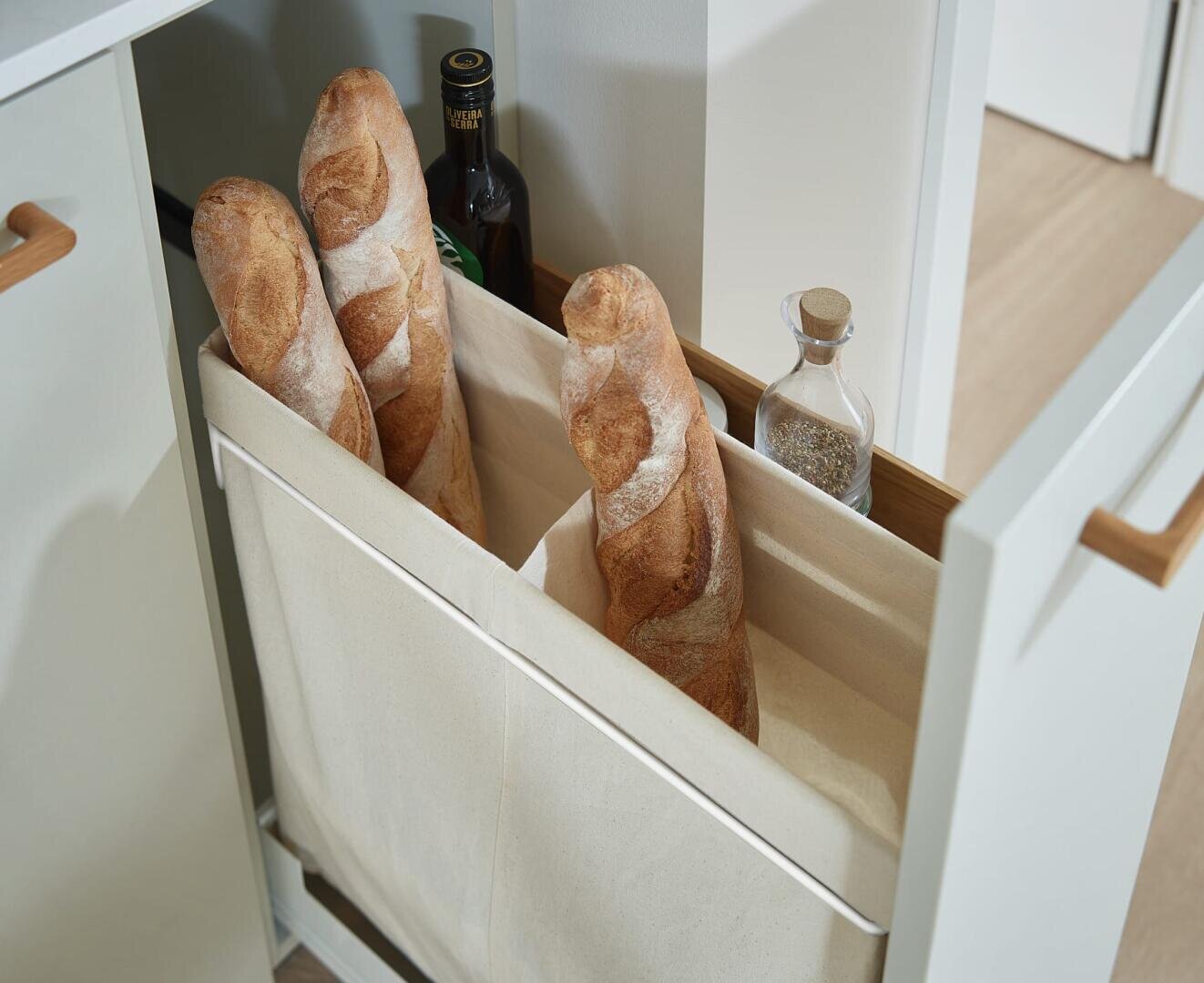Drei Baguettes und zwei Flaschen, eine mit Olivenöl und eine mit Gewürzen, sind in einer modernen Küche in einer ausziehbaren Stoffschublade untergebracht.