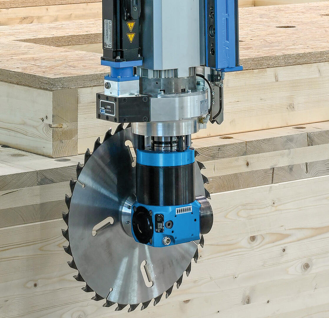 Nahaufnahme eines industriellen Kreissägeblatts, das an einer Maschine befestigt ist und über gestapelten hellen Holzplatten in einer Werkstatt steht.